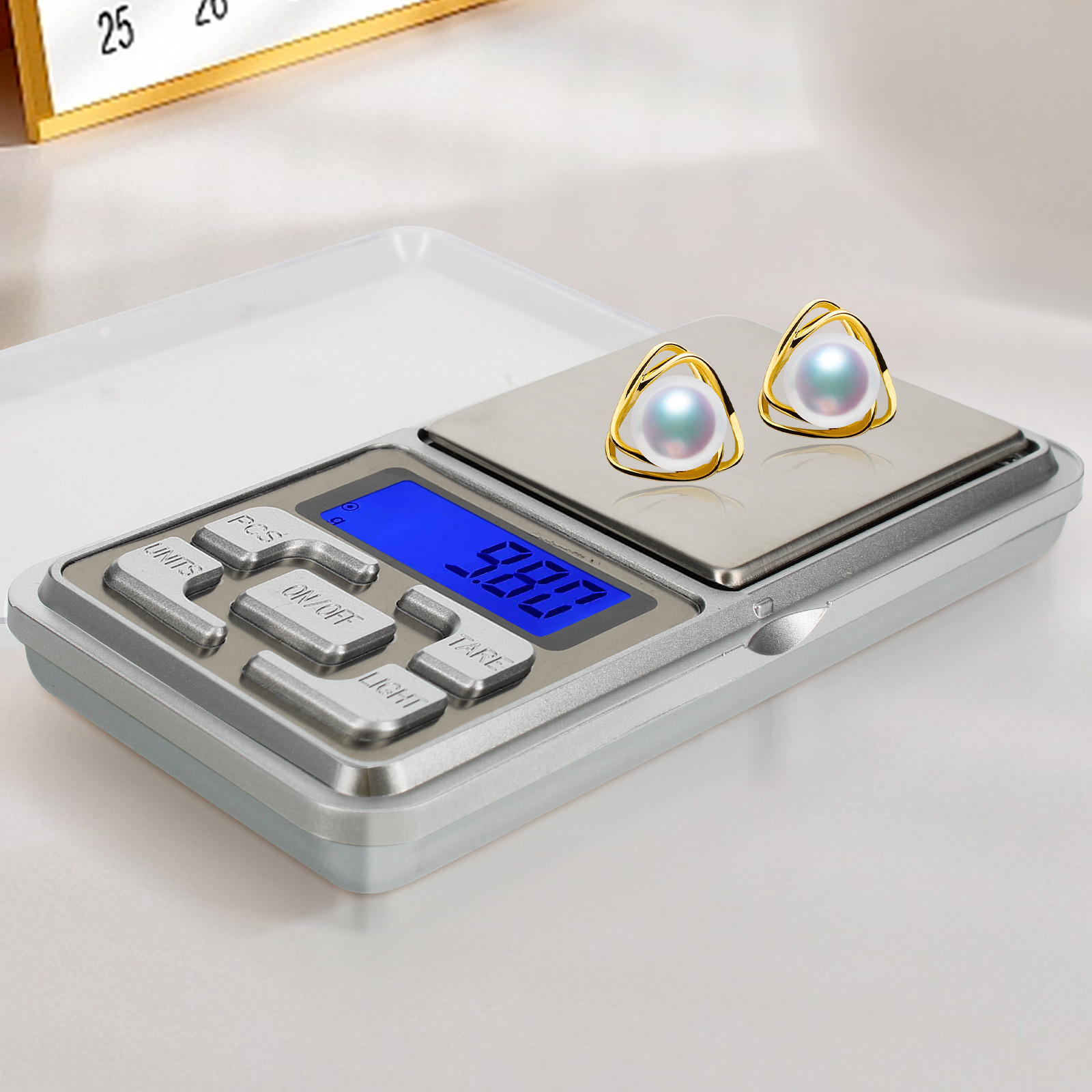 Eine Waage mit Ohrringen. Die Waage zeigt 9,80 an. Ohrringe sind Gold und Perle.
