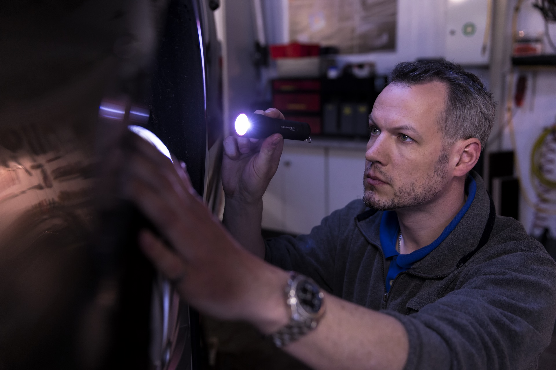 Mężczyzna sprawdza samochód. Trzyma latarkę, patrząc na powierzchnię samochodu.
