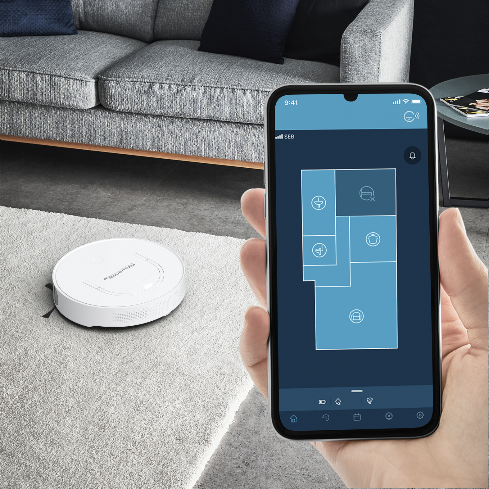 Aspirapolvere robotico bianco su un tappeto chiaro. Un telefono mostra una planimetria, indicando il progresso.