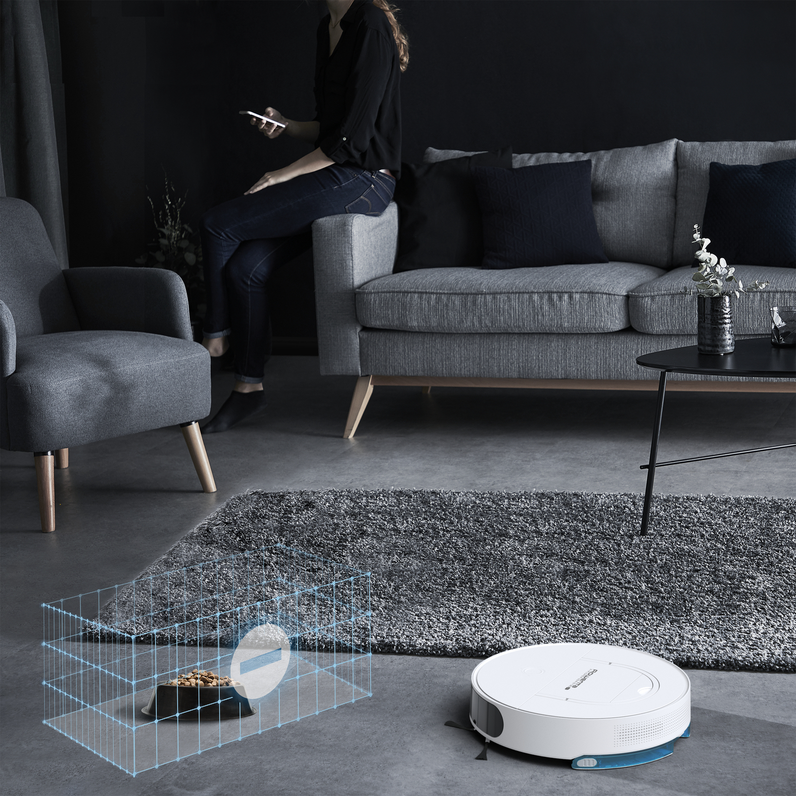 Un robot aspirapolvere, una donna con un telefono, una gabbia con una ciotola in una stanza.
