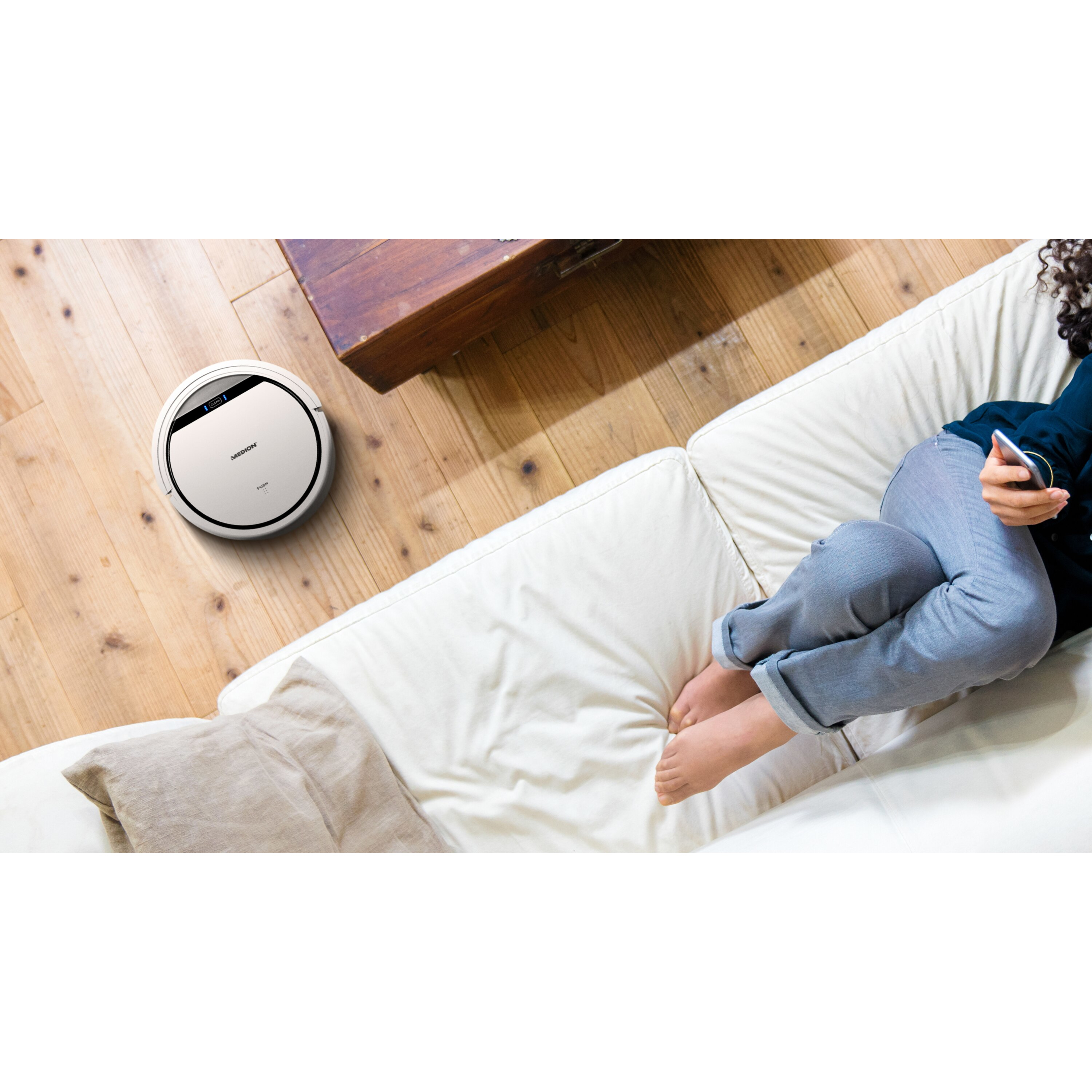 Una aspiradora robot limpia una habitación, una persona se relaja en un sofá.