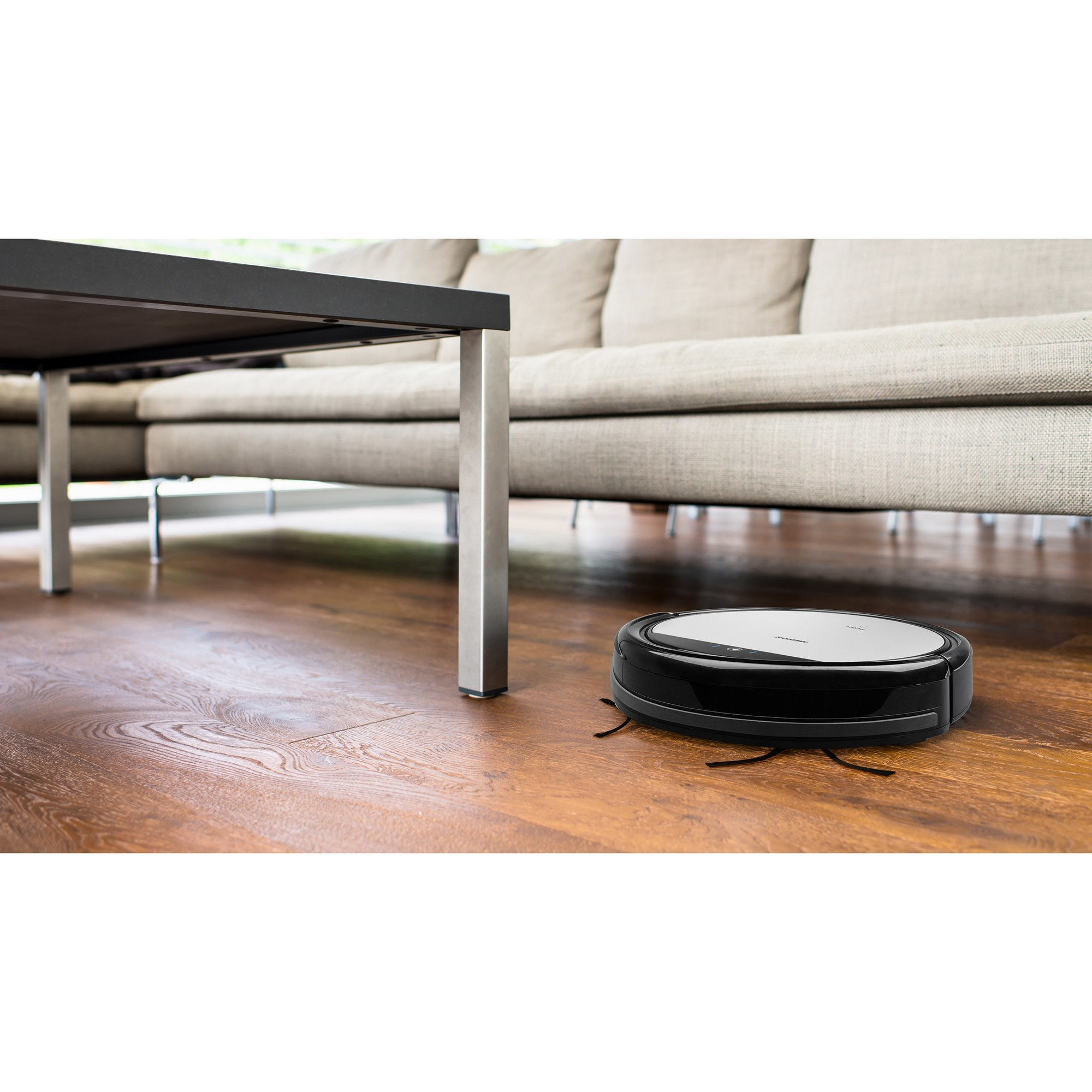 Ein schwarzer Roboter-Staubsauger auf einem Holzboden. Ein Sofa und ein Tisch sind ebenfalls im Bild.