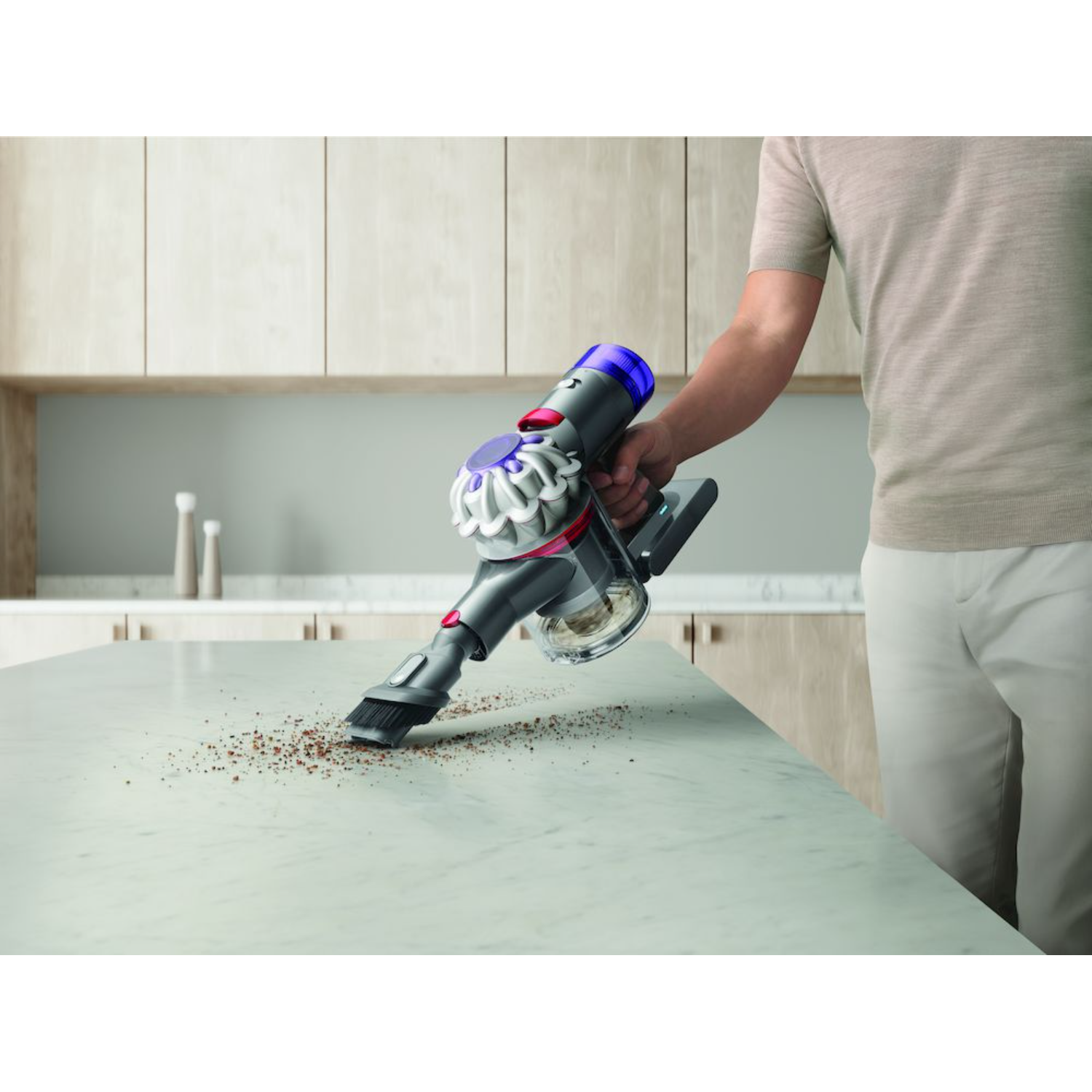Eine Person reinigt eine weiße Arbeitsplatte mit einem Dyson Staubsauger.