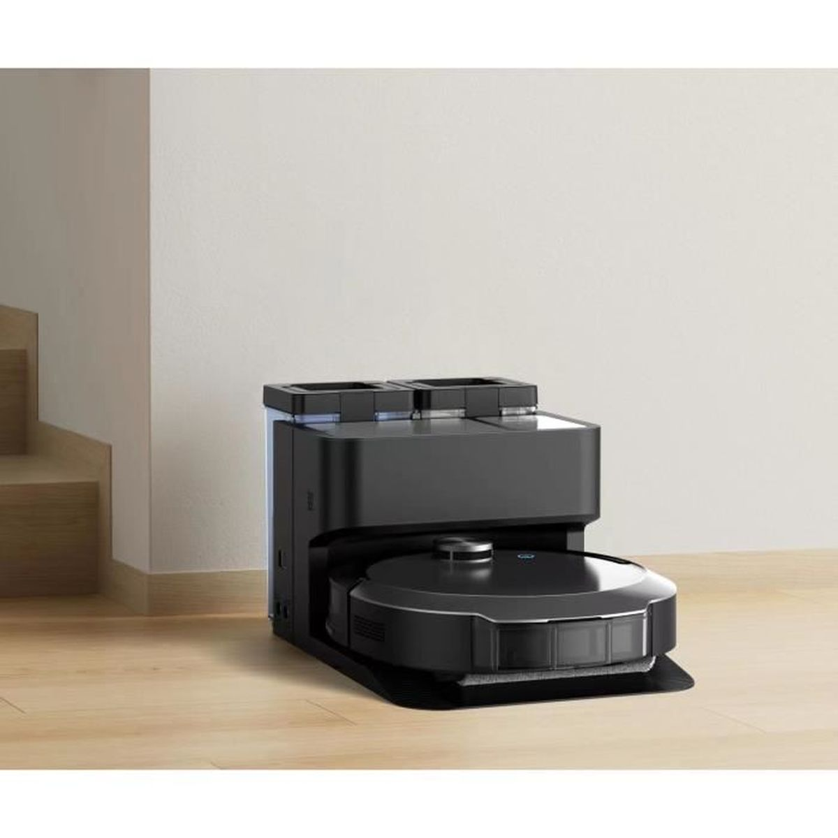 Czarny robot odkurzający i stacja ładująca. Drewniana podłoga i biała ściana.