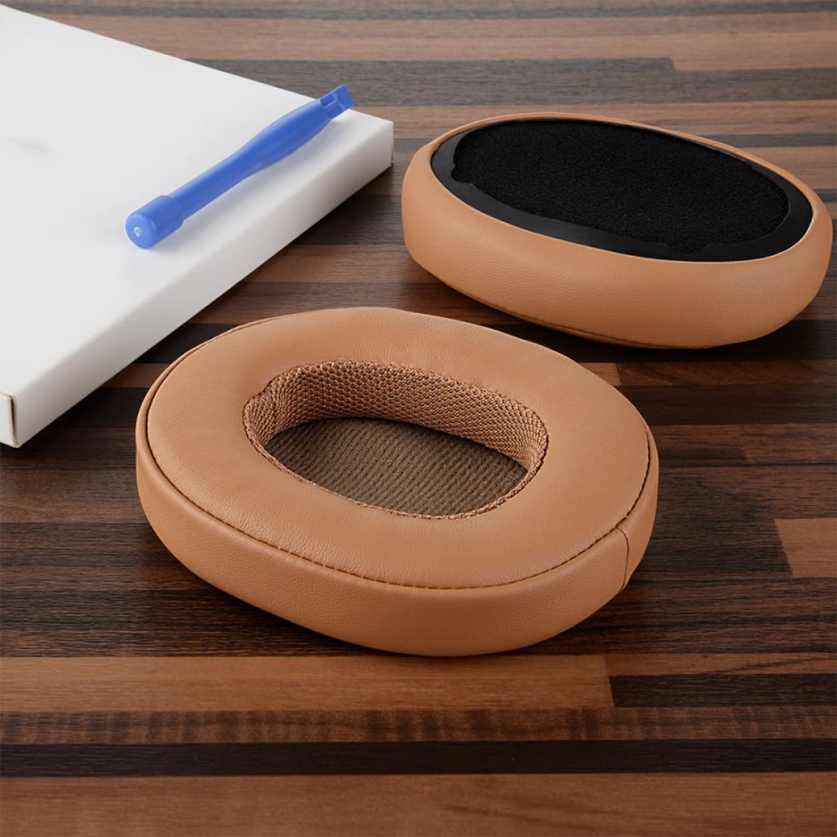 Hoofdtelefoon oorkussens, bruin leer, op houten tafel met schroevendraaier en witte doos.