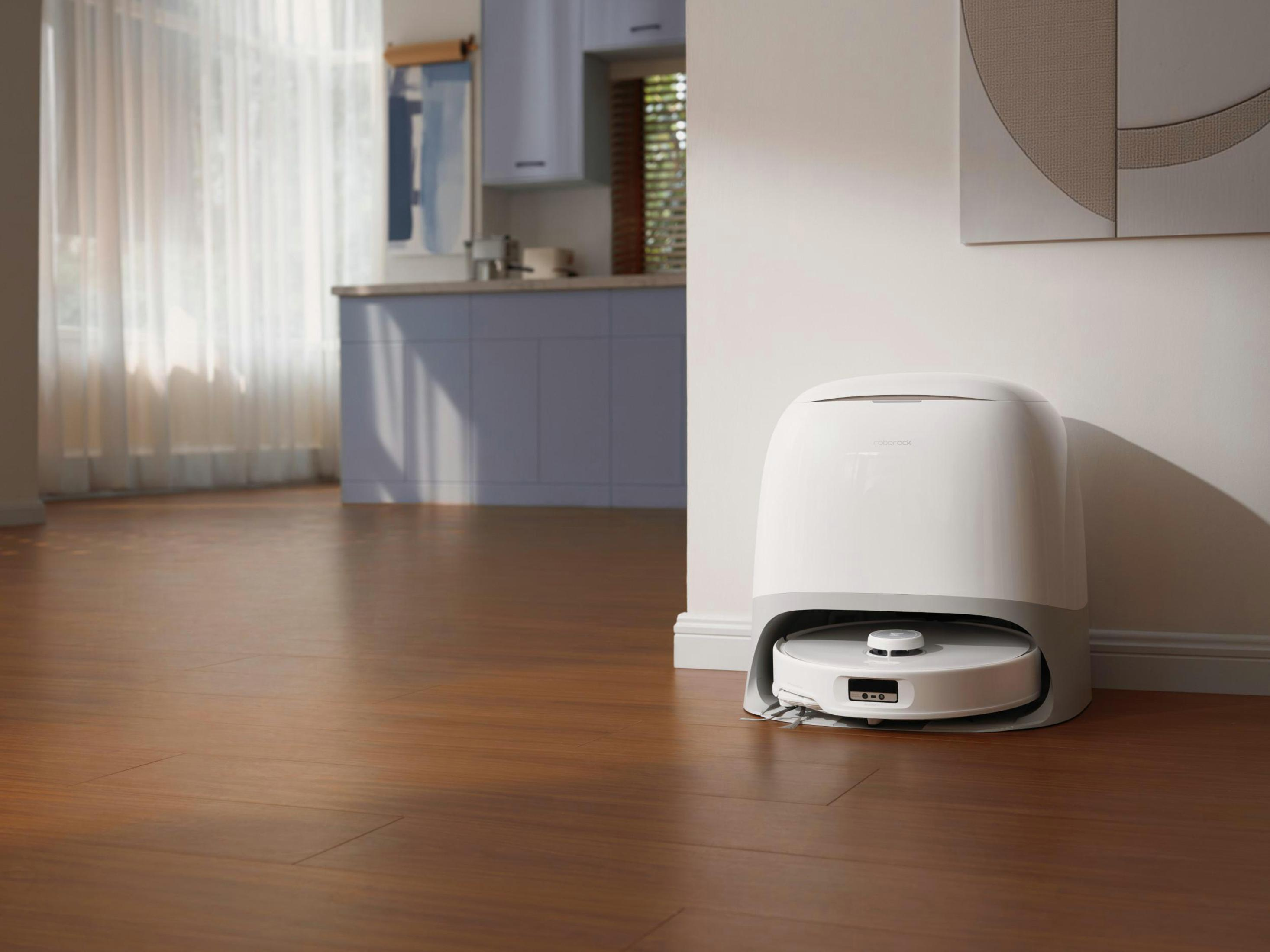 Ein weißer Roboter-Staubsauger und eine Ladestation auf einem Holzboden in einem Raum.