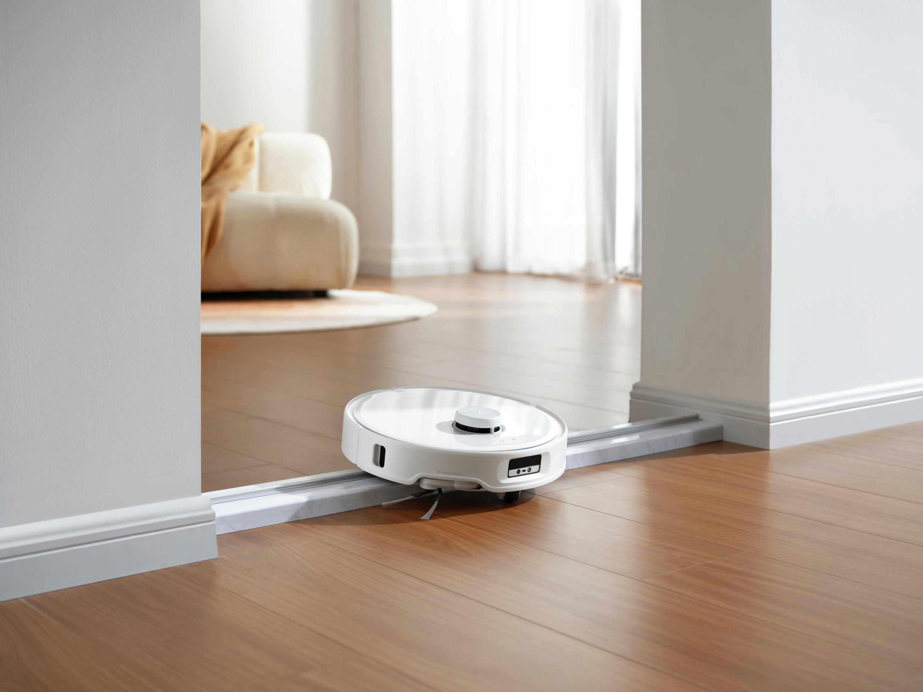 Weißer Roboter-Staubsauger in einem Raum. Er befindet sich auf einer Schiene und bewegt sich. Weiße Wände und Holzboden.