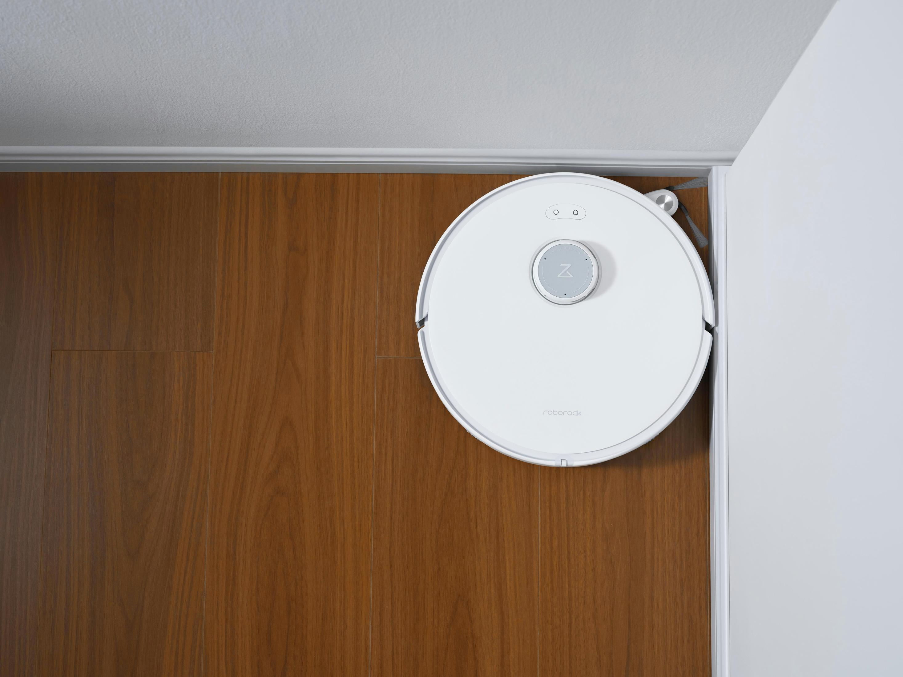 Ein weißer Roboter-Staubsauger auf einem Holzboden neben einer Wand. Das Roborock-Logo ist sichtbar.