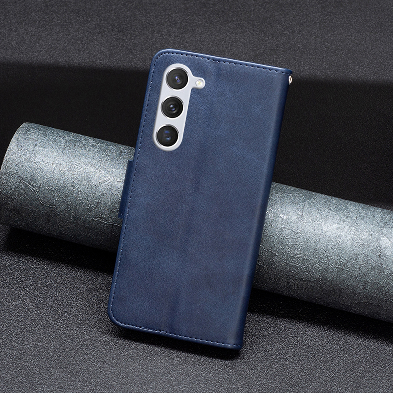 Blauwe leren telefoonhoes met een camerabult. De hoes is gesloten. Donkere achtergrond.