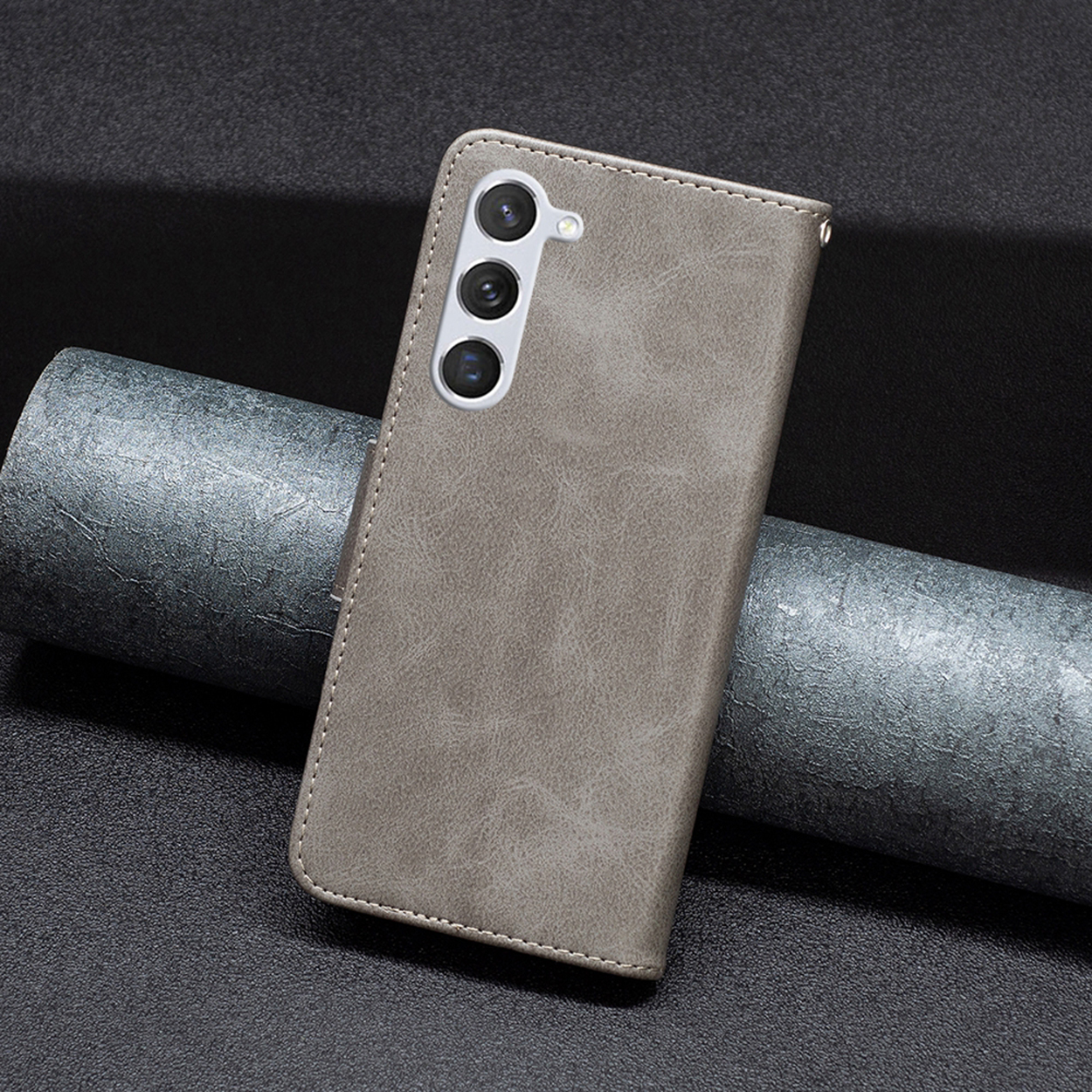Une coque de téléphone grise avec un téléphone à l'intérieur, montrée sur une surface sombre. On dirait du cuir.