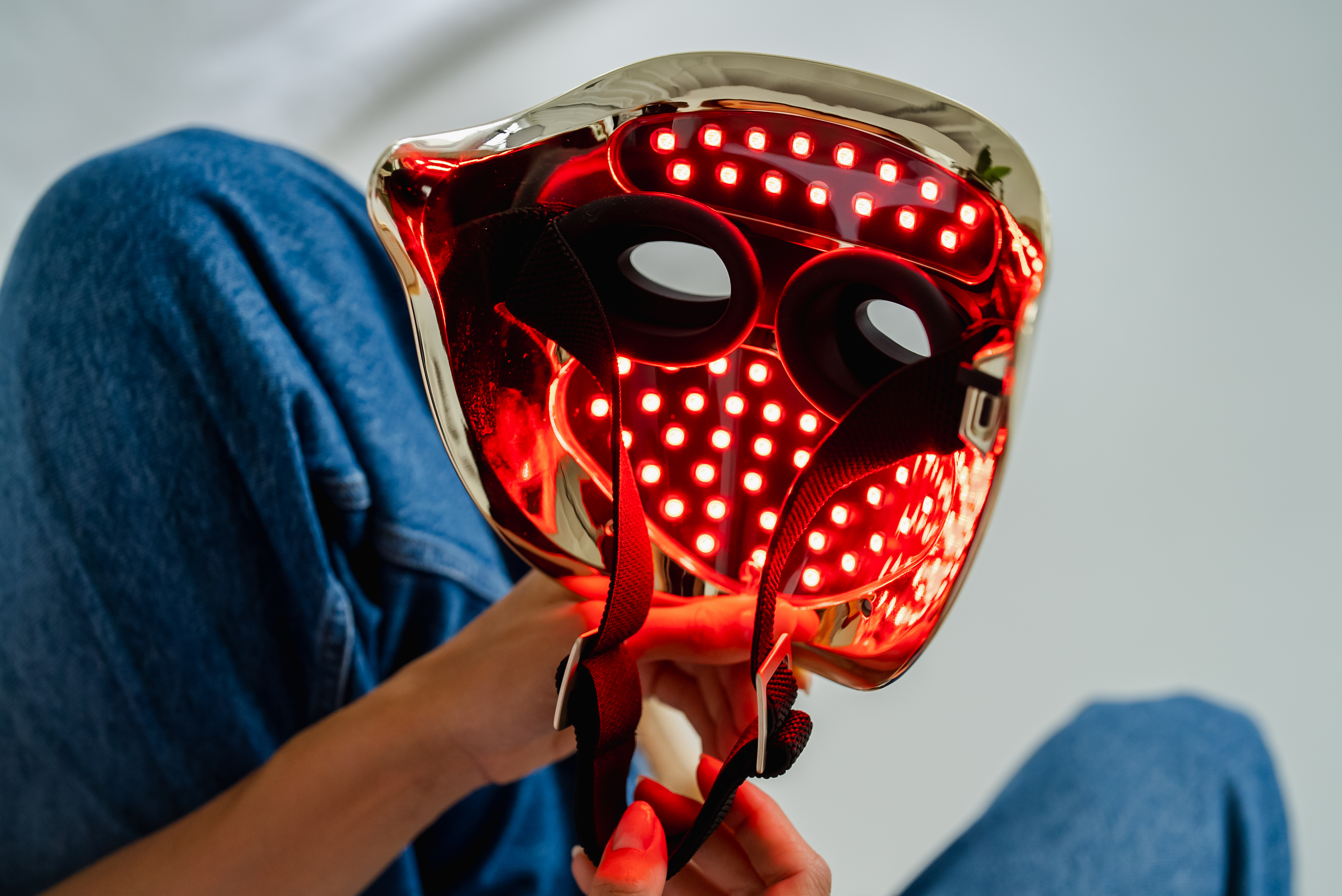 Persona che tiene una maschera per la terapia della luce rossa. La maschera ha molte piccole luci rosse.
