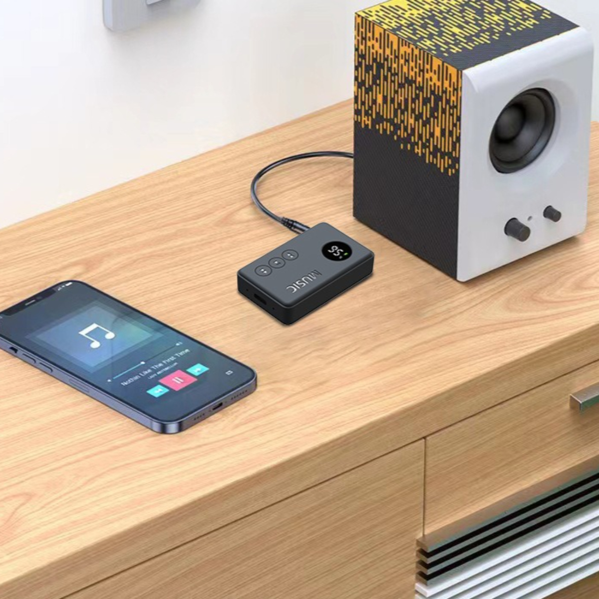 Schwarzes Gerät mit Bildschirm, verbunden mit einem Musik abspielenden Telefon und einem Lautsprecher. Alles auf Holzoberfläche.