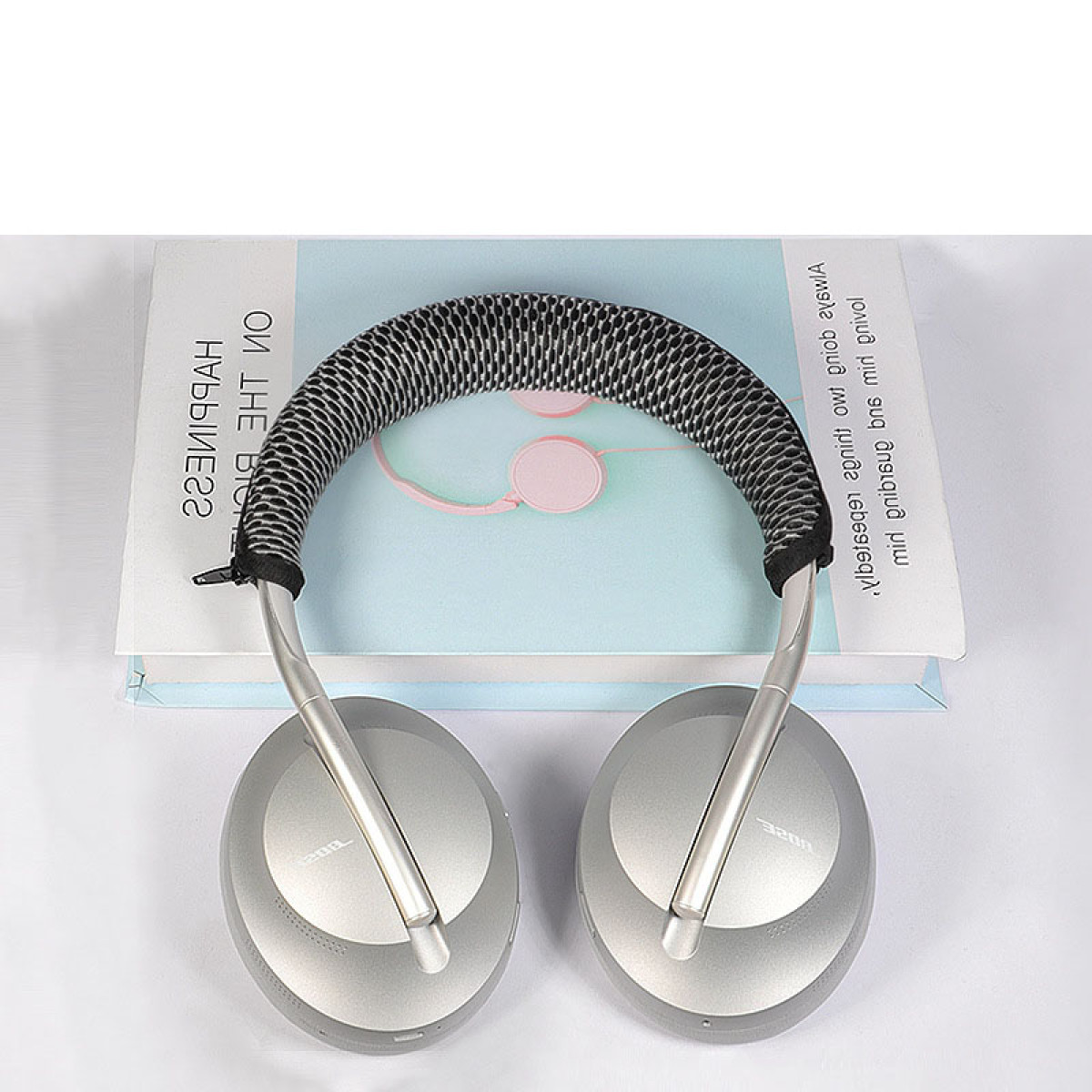 Srebrne słuchawki z czarnym pałąkiem z siatki, spoczywające na książce z tekstem, na białej powierzchni.