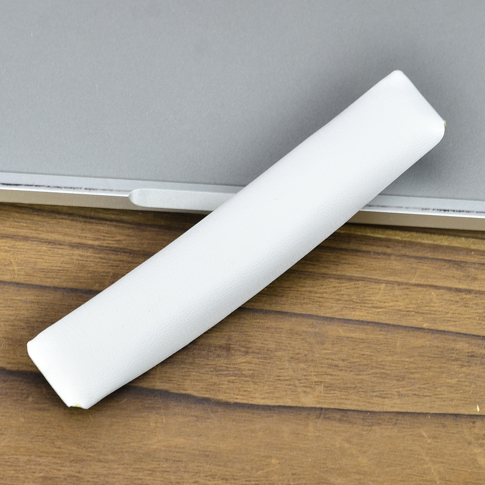 Biała, wyściełana poduszka na pałąk spoczywa na jasnoszarym laptopie, na drewnianym stole.