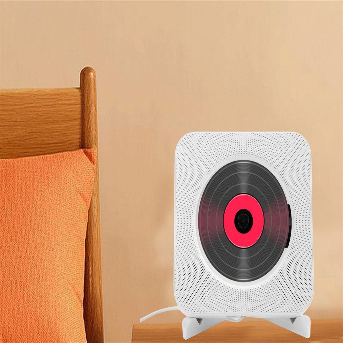 Weißer, an der Wand befestigter CD-Player mit roter Mitte, auf Holztisch neben orangefarbenem Kissen und Stuhl.