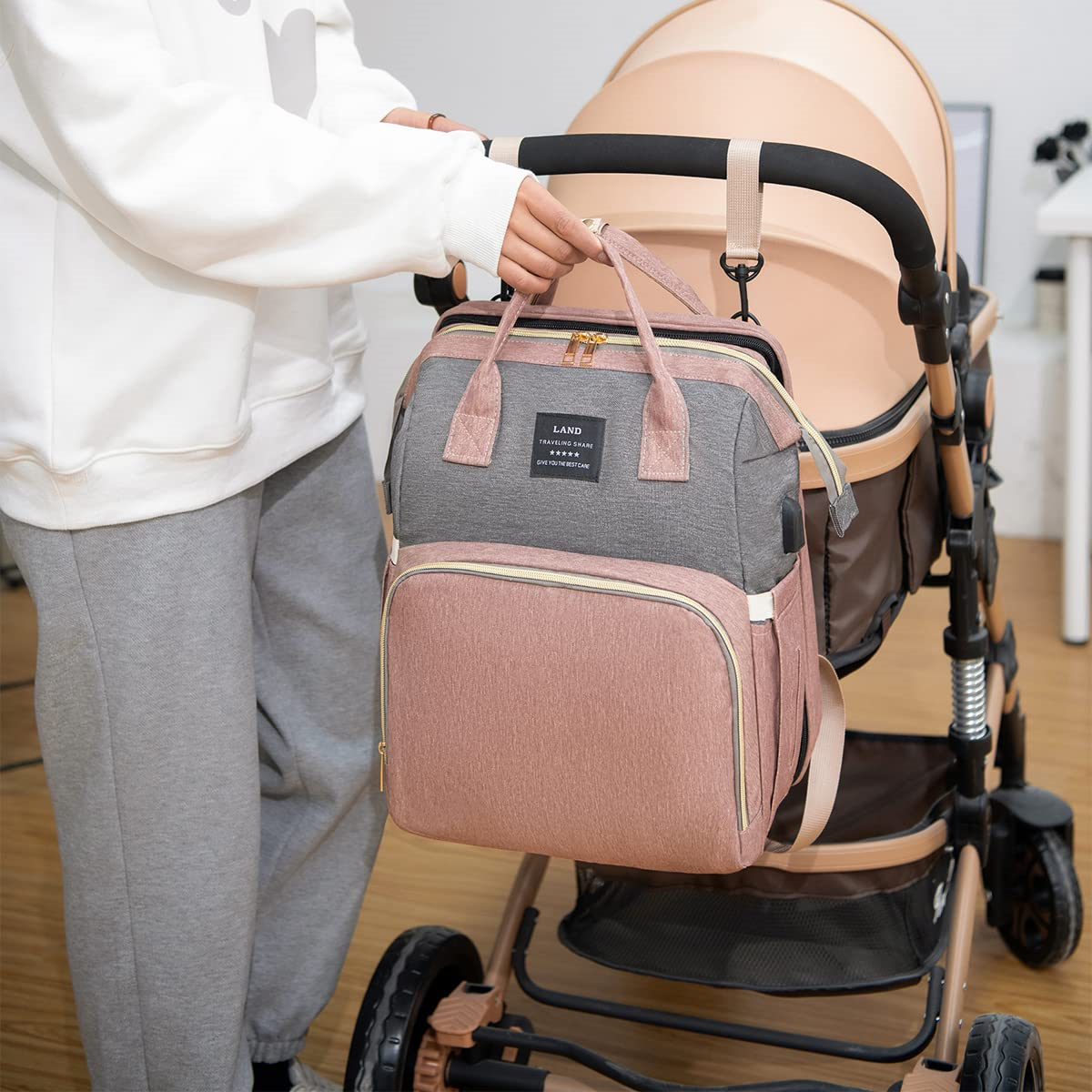 Eine Frau hält eine Wickeltasche, die an einem Kinderwagen befestigt ist. Die Tasche ist rosa und grau.