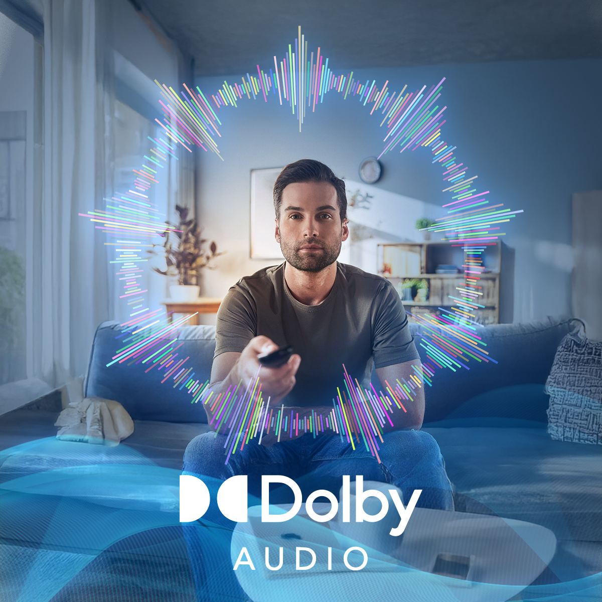 Mężczyzna na kanapie z pilotem, ogląda TV. Logo Dolby Audio w lewym dolnym rogu.