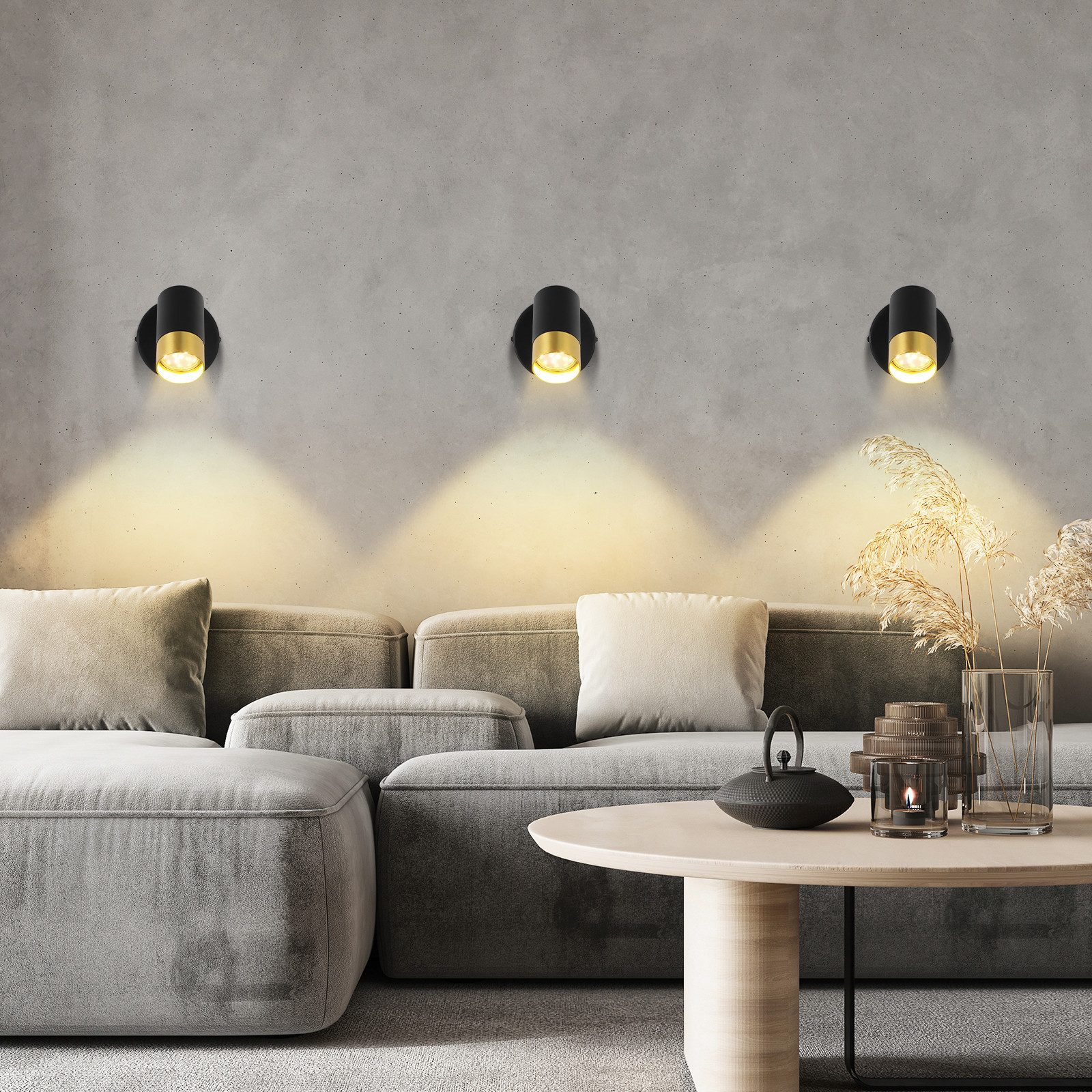 Tre lampade da parete nere e oro su un muro grigio sopra un divano grigio e un tavolo di legno.
