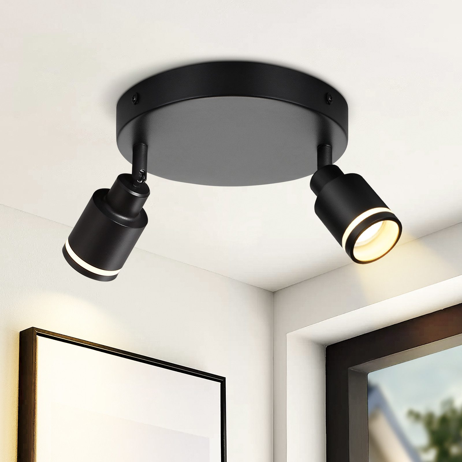 Due faretti neri montati su un soffitto bianco. La stanza è moderna con un dipinto.