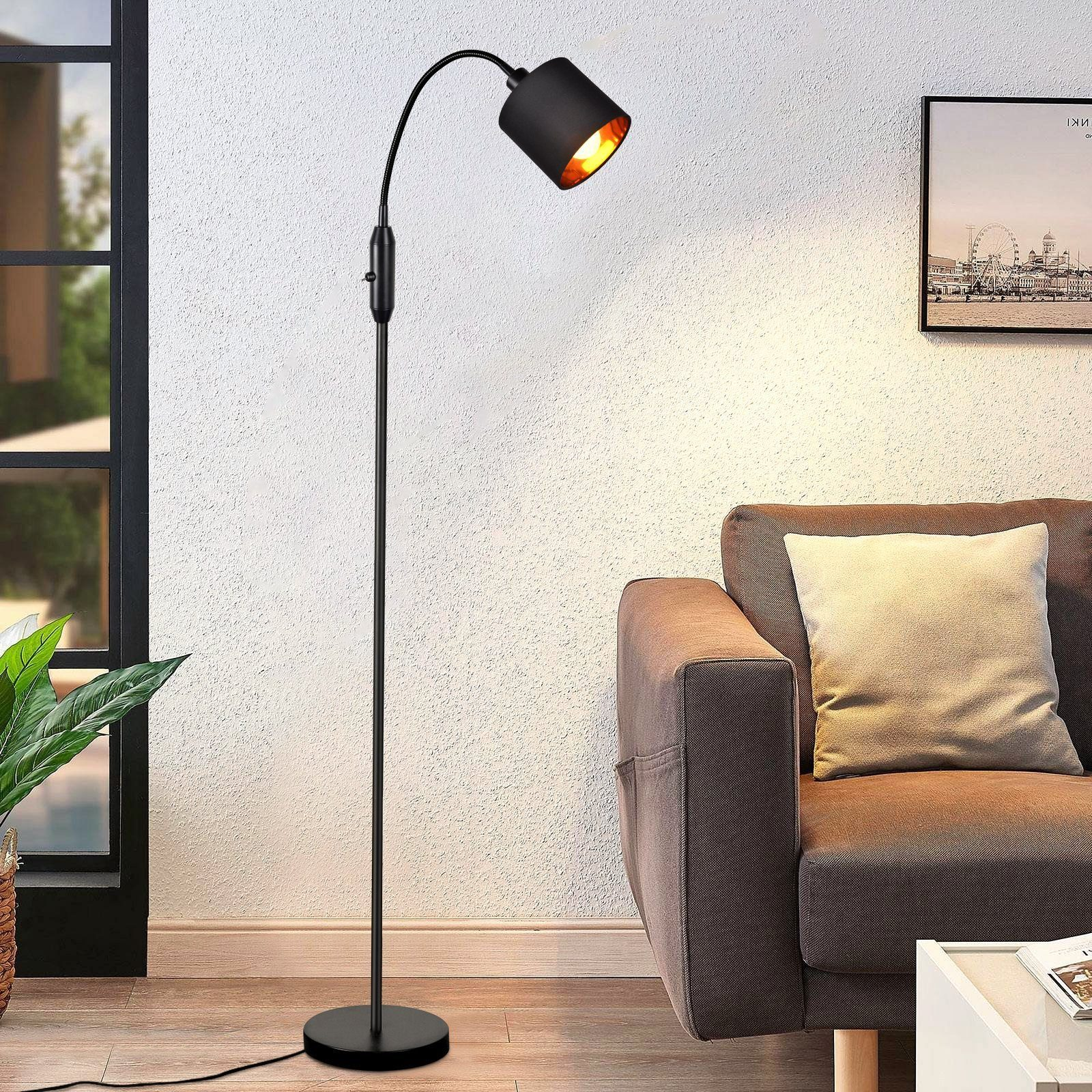 Eine schwarze Stehlampe mit gebogenem Arm und Lampenschirm. Die Lampe steht in einem Raum mit Sofa und Gemälde.