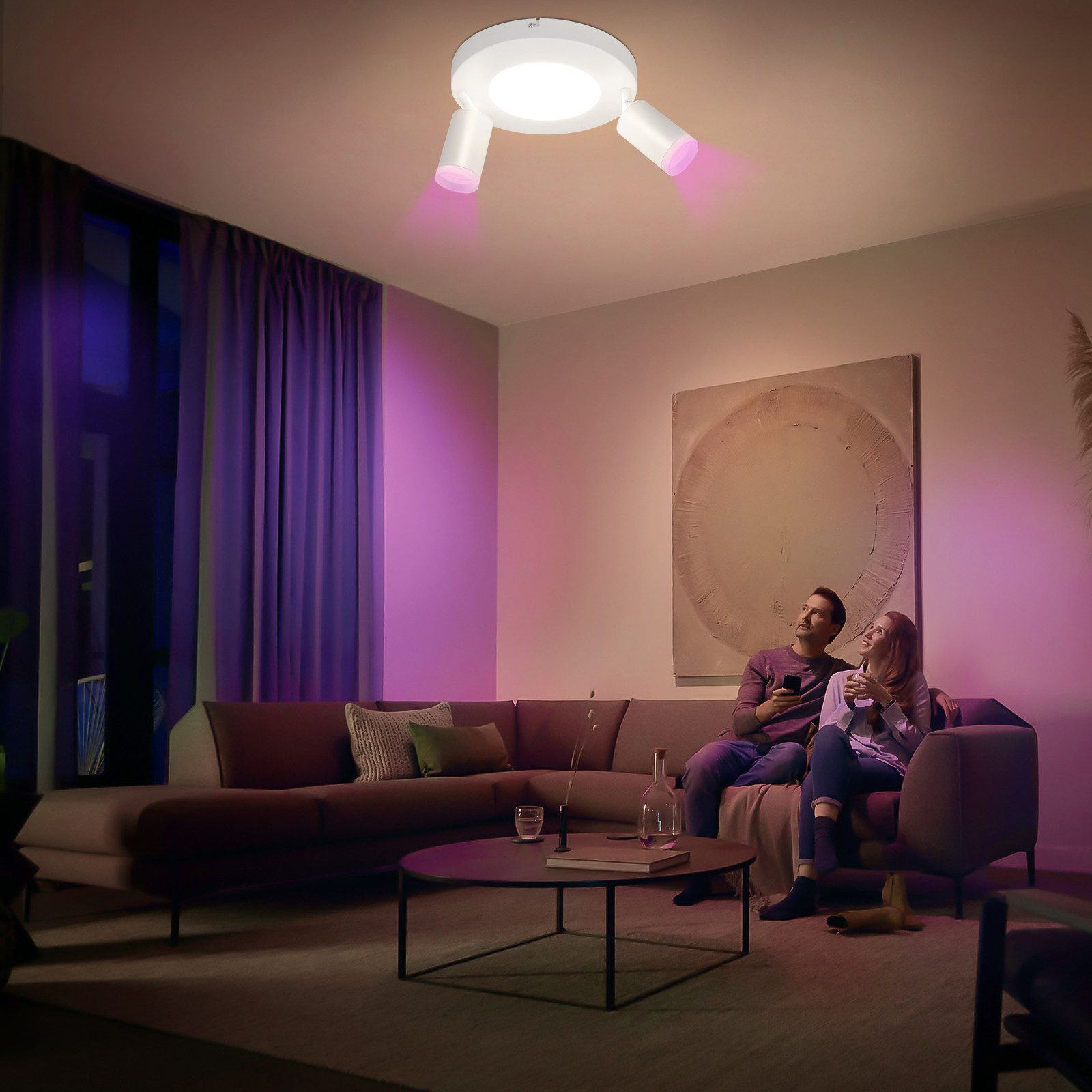 Una coppia su un divano, una luce a soffitto con raggi rosa che illuminano la stanza.