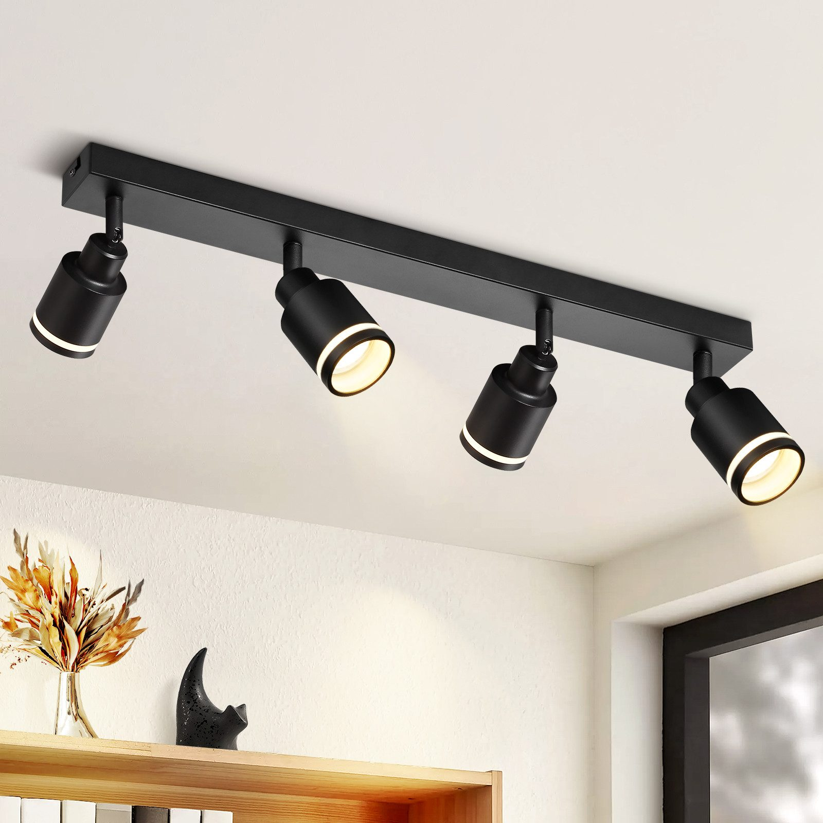 Faretti da soffitto neri su un soffitto bianco, con un vaso e decorazioni su uno scaffale.