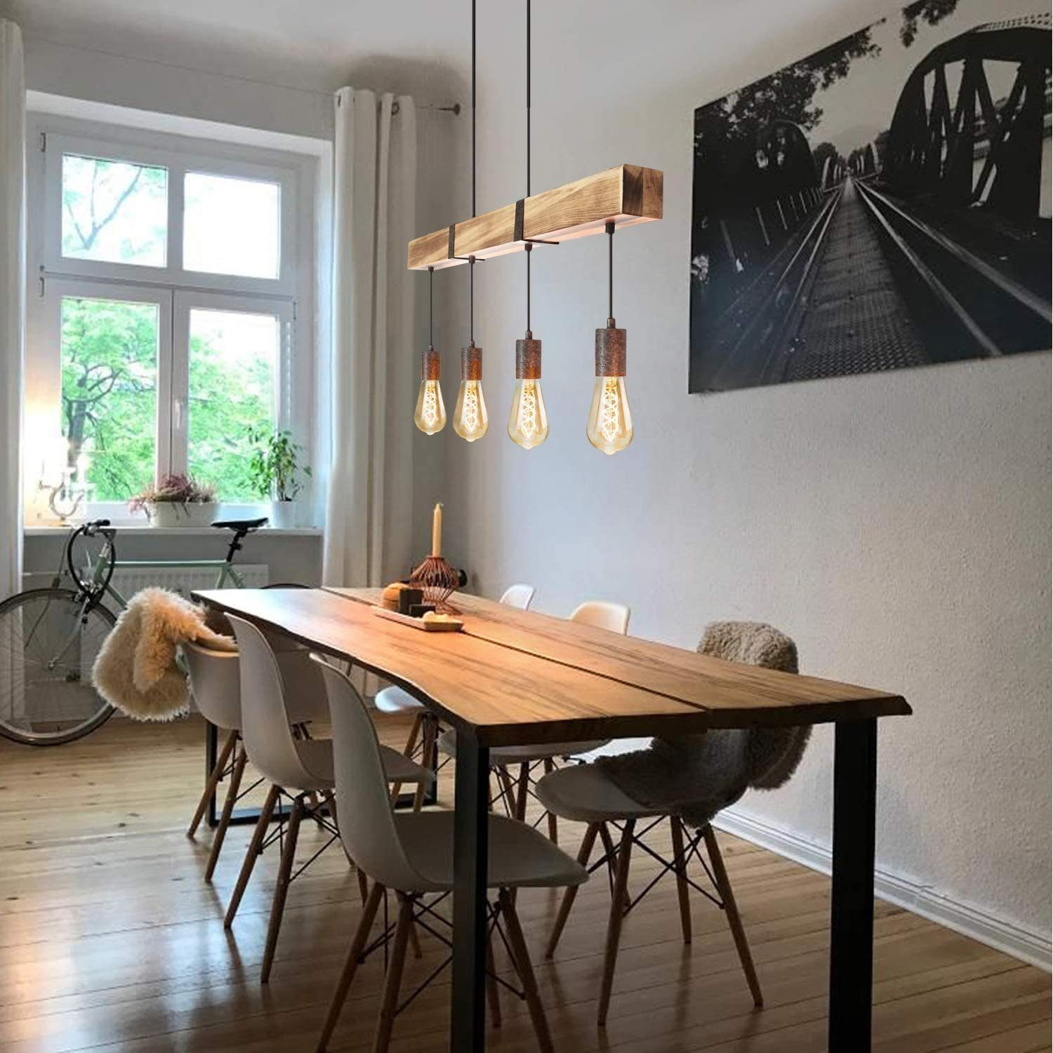 Sala da pranzo con tavolo in legno, sedie e luci sospese. Una finestra e opere d'arte sono visibili.