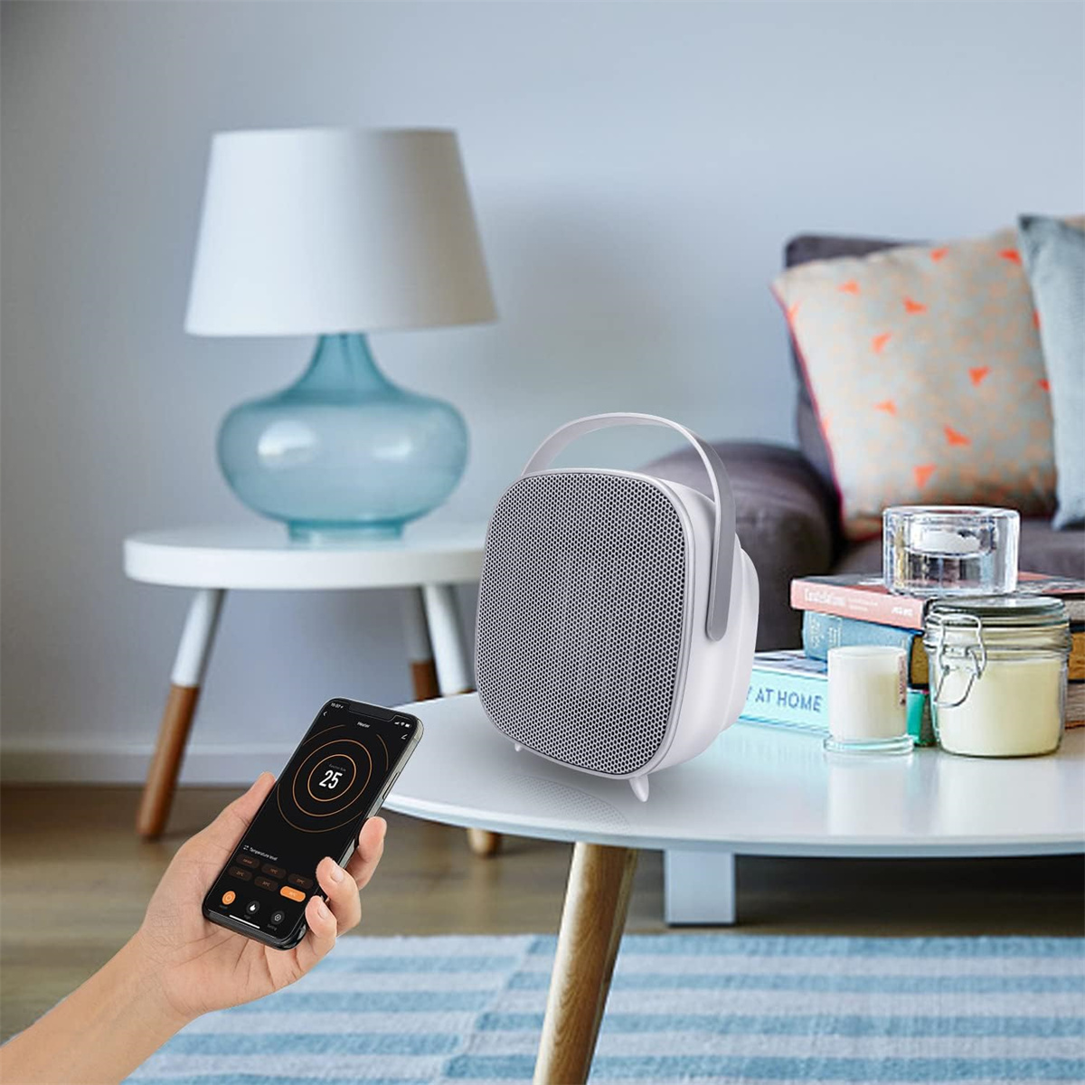 Eine Hand steuert einen Heizlüfter per Telefon. Der Heizlüfter und eine Lampe stehen auf einem Tisch.