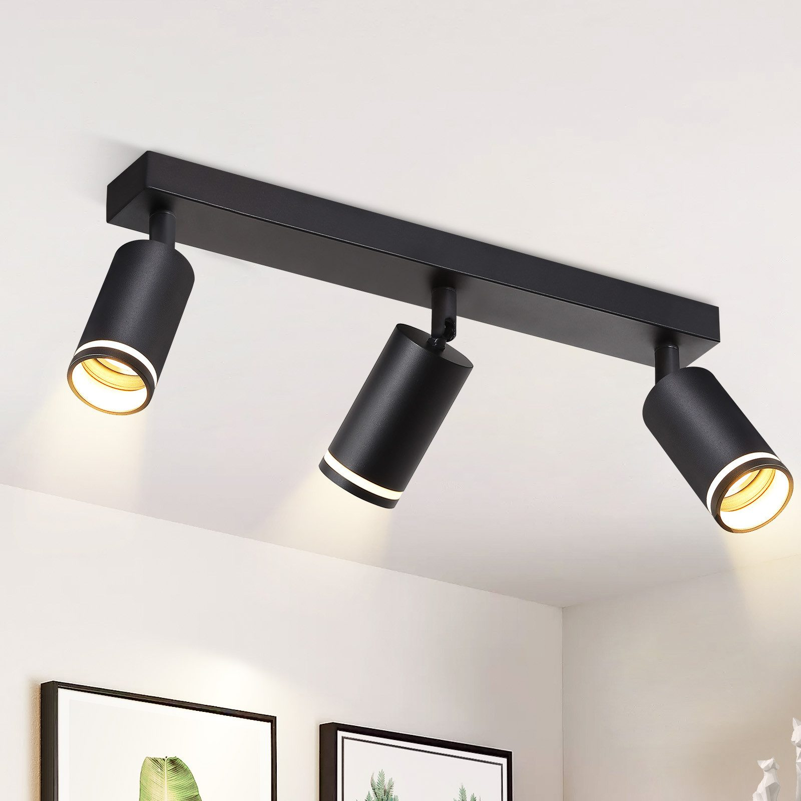 Un apparecchio di illuminazione nero a soffitto con tre luci cilindriche. Le luci sono accese.