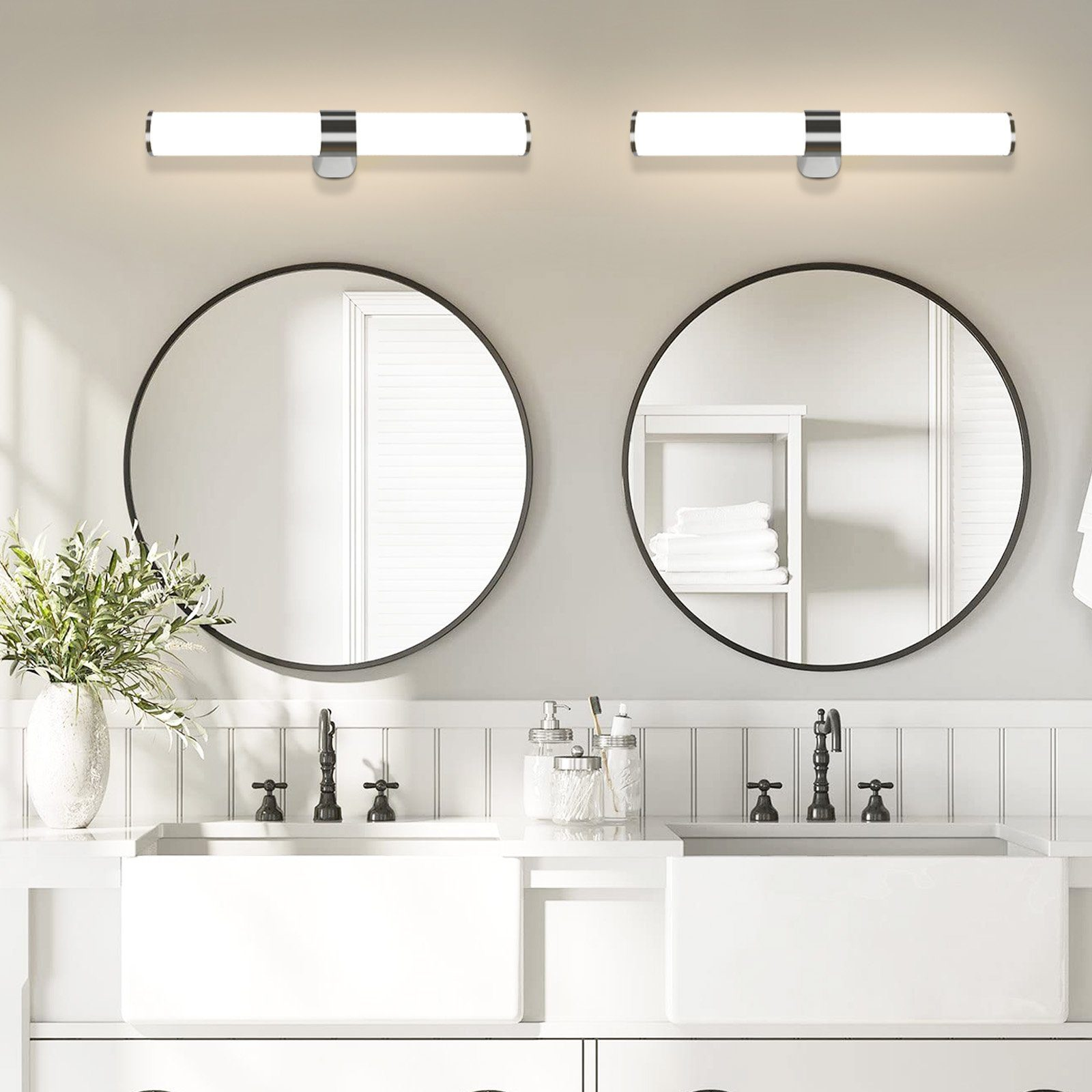 Badezimmer mit zwei runden Spiegeln und zwei beleuchteten Waschtischleuchten. Weiße Waschbecken und Deko.