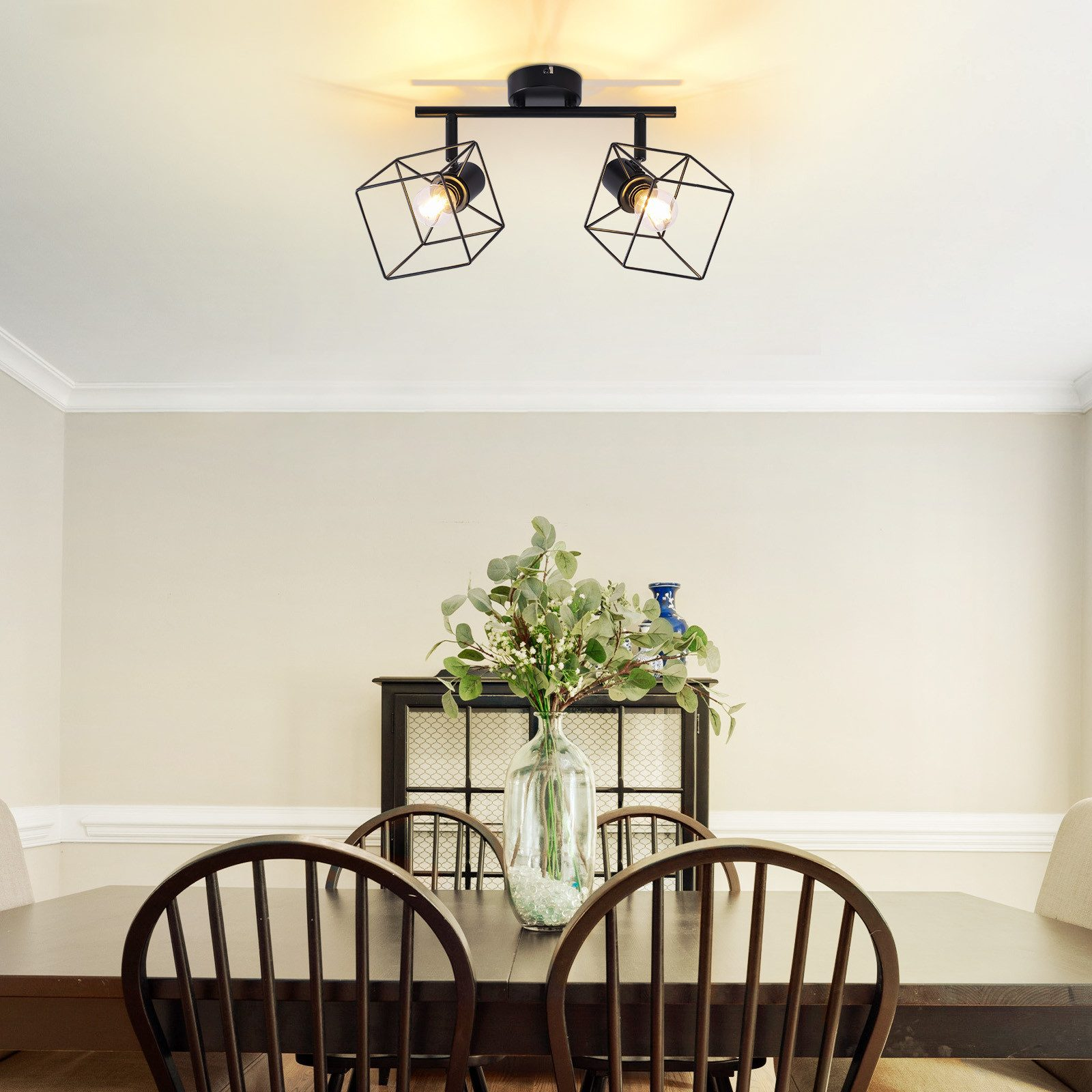 Sala da pranzo con luci geometriche, tavolo, sedie e vaso.