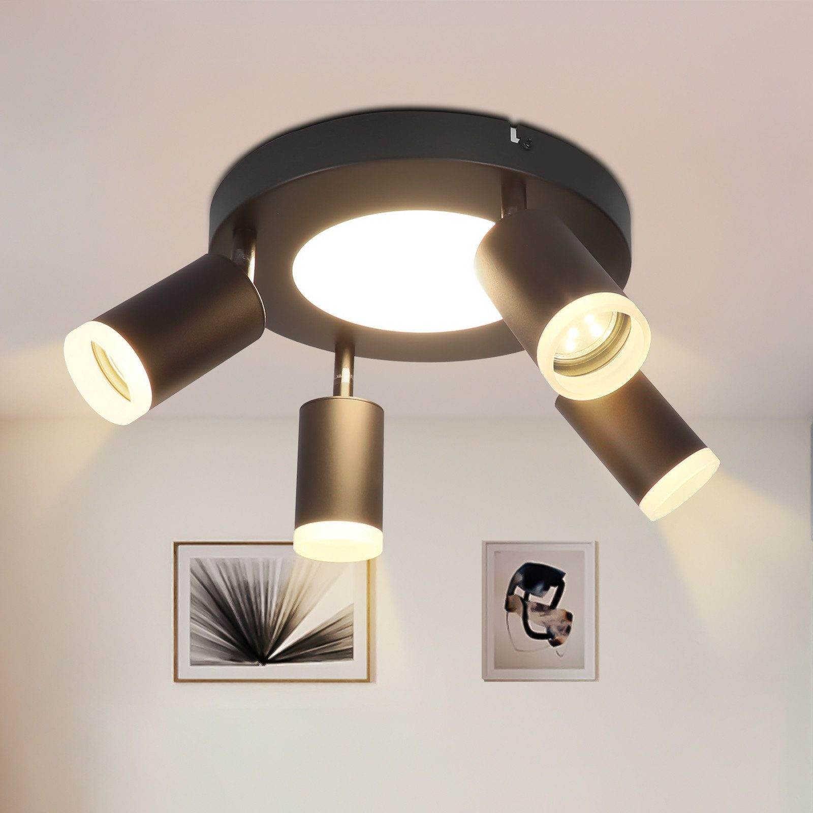 Faretto da soffitto nero con quattro luci regolabili, centrato su un soffitto bianco. Due opere d'arte sul muro.