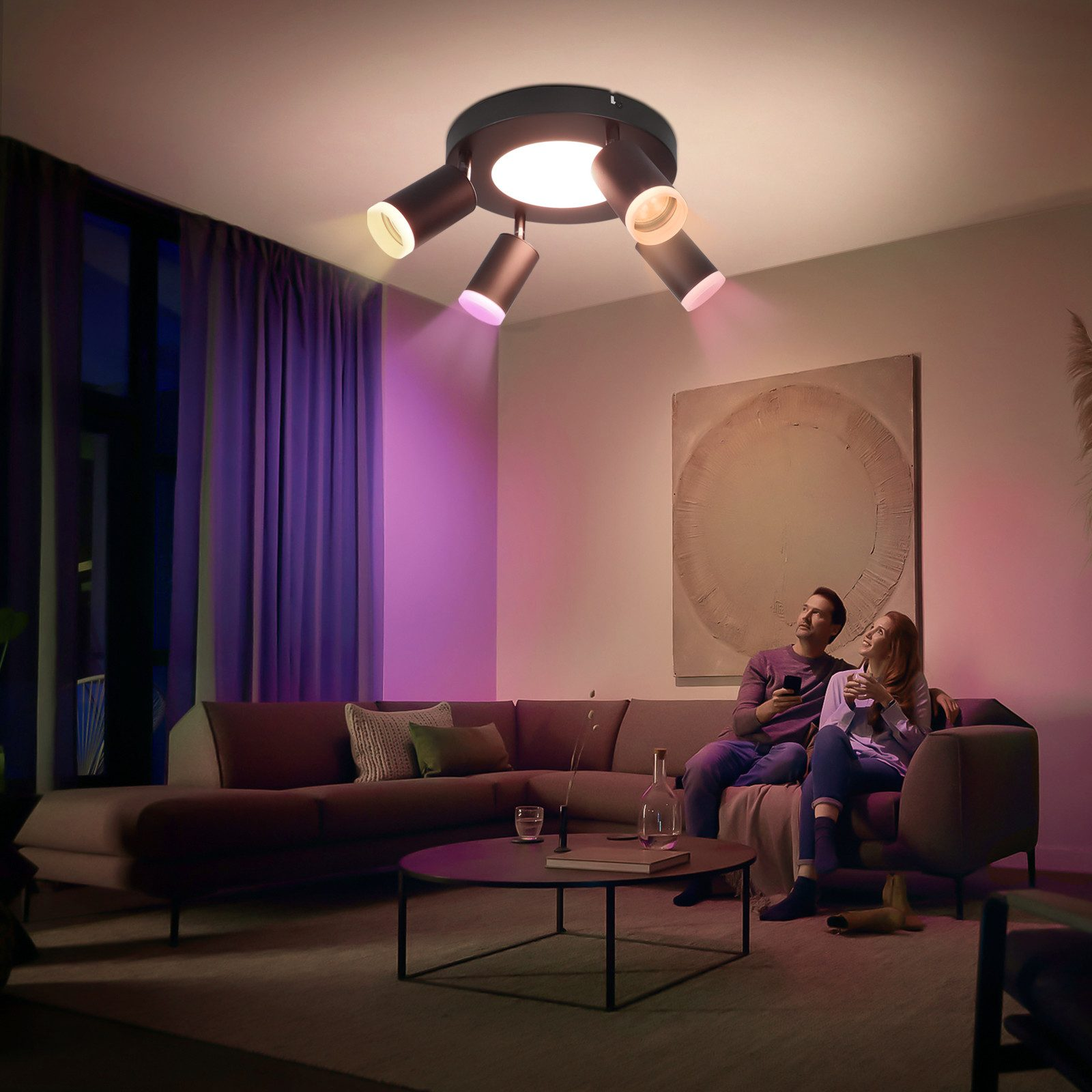 Un soggiorno con una coppia su un divano e una luce a soffitto con faretti colorati. La stanza ha luci viola.