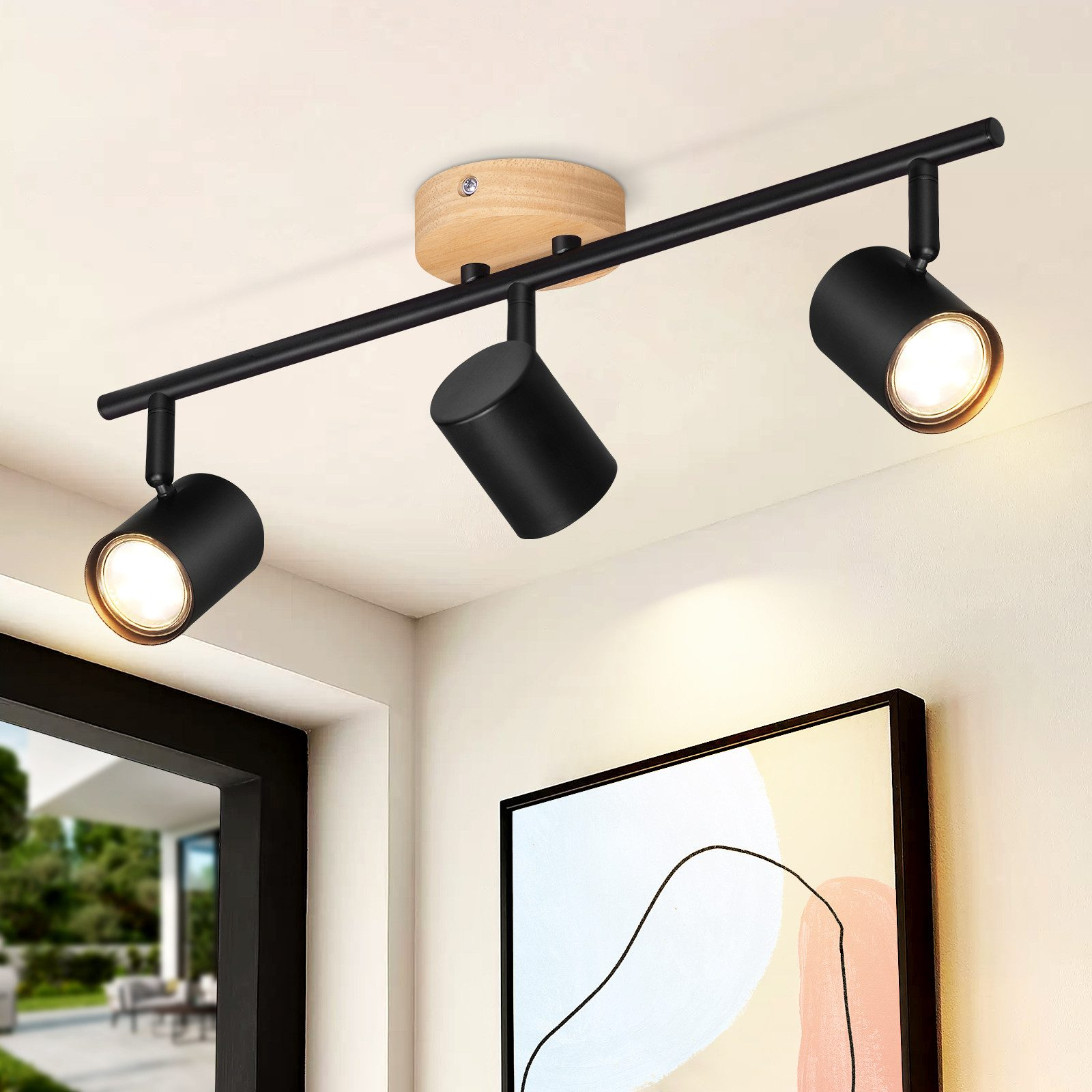 Illuminazione a binario nera con tre faretti su un soffitto bianco. Un quadro è appeso sotto.