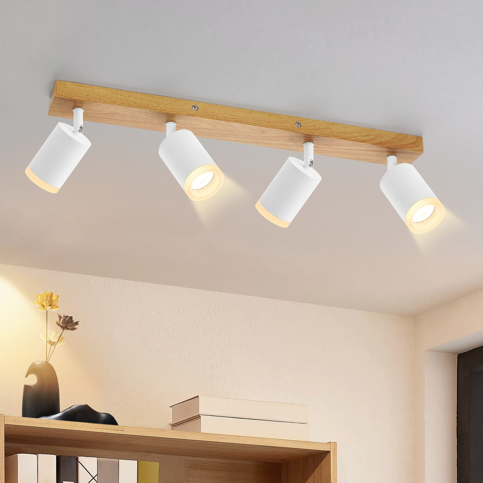 Lampada da soffitto con quattro faretti bianchi su trave in legno. Vaso di fiori sotto.