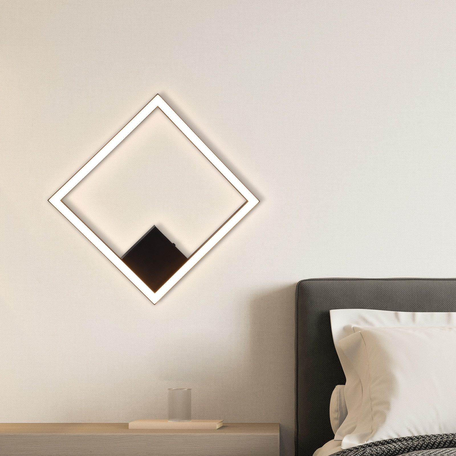 Lampada da parete: quadrato bianco con centro nero, montato su una parete beige accanto a un comodino.