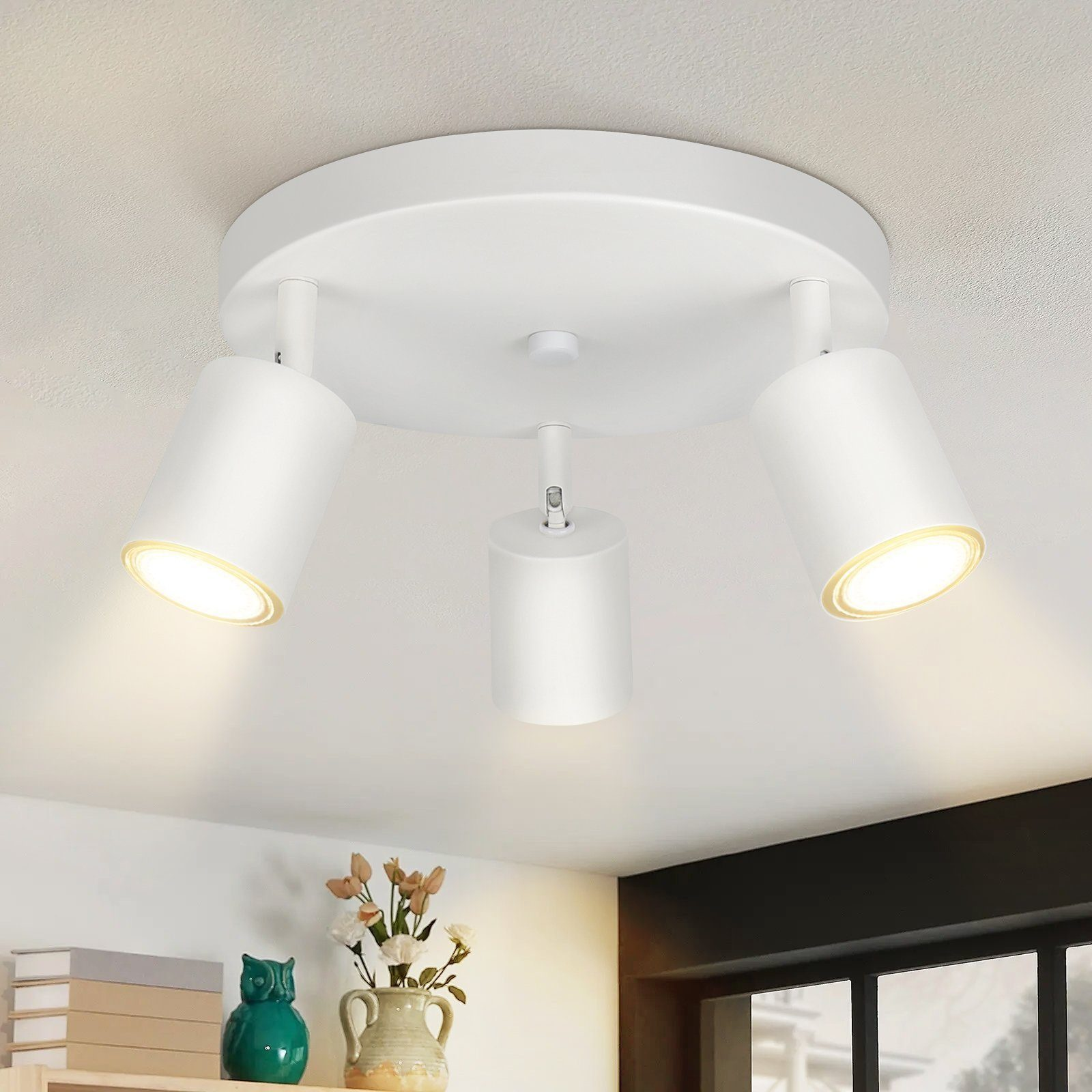 Tre faretti bianchi montati su un soffitto bianco. Le luci sono angolate verso il basso. Ci sono fiori sotto.