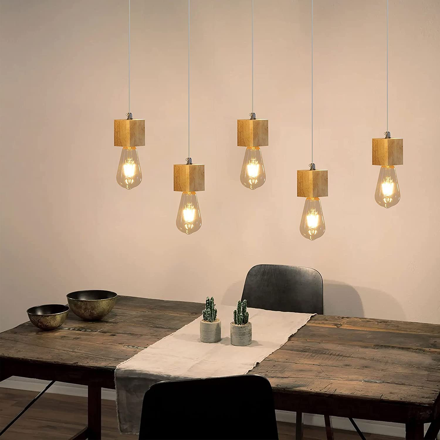 Pięć drewnianych lamp wiszących z żarówkami Edisona wiszących nad stołem z dekoracjami.