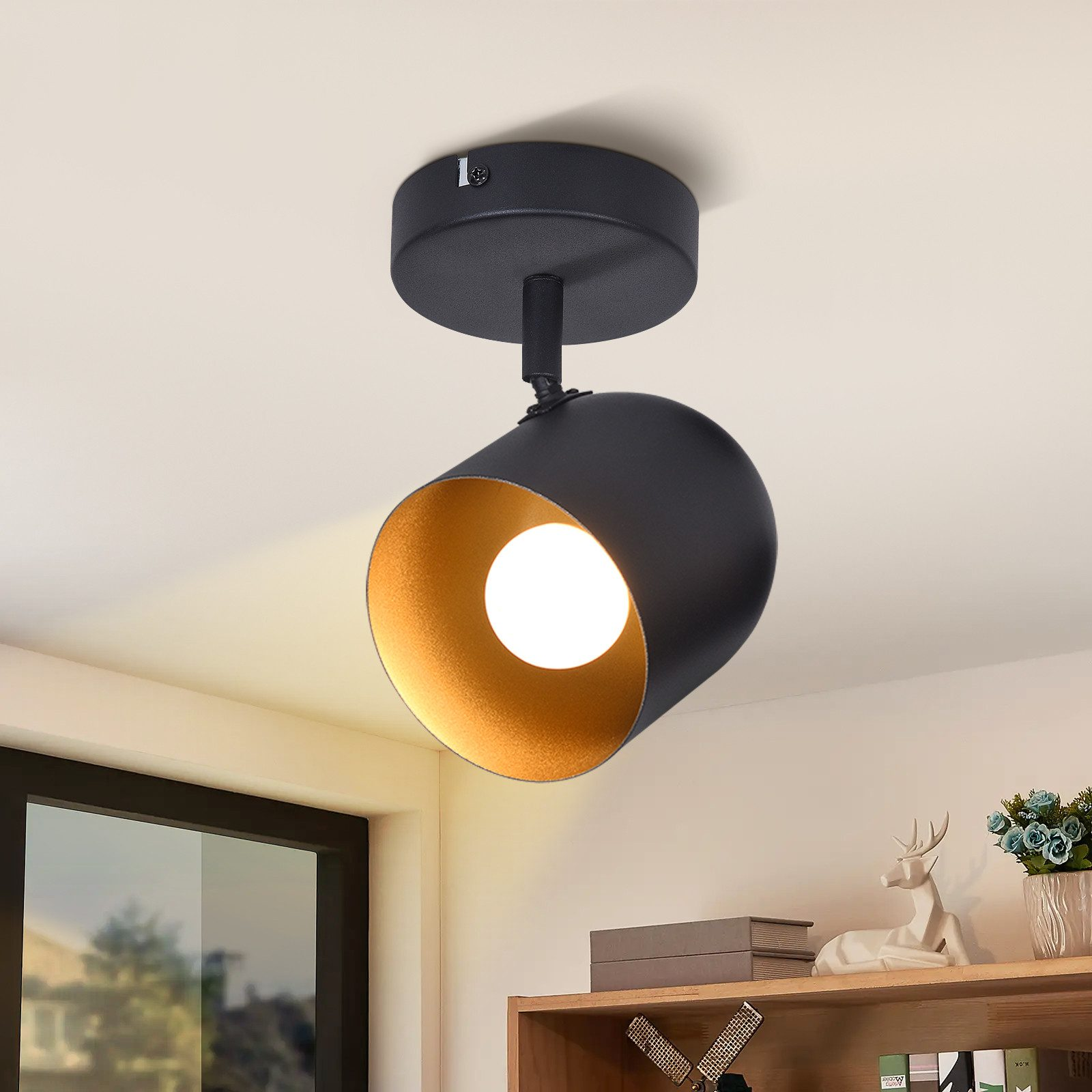 Faretto da soffitto nero con interno dorato. La luce illumina una stanza con ripiano e statua di cervo.