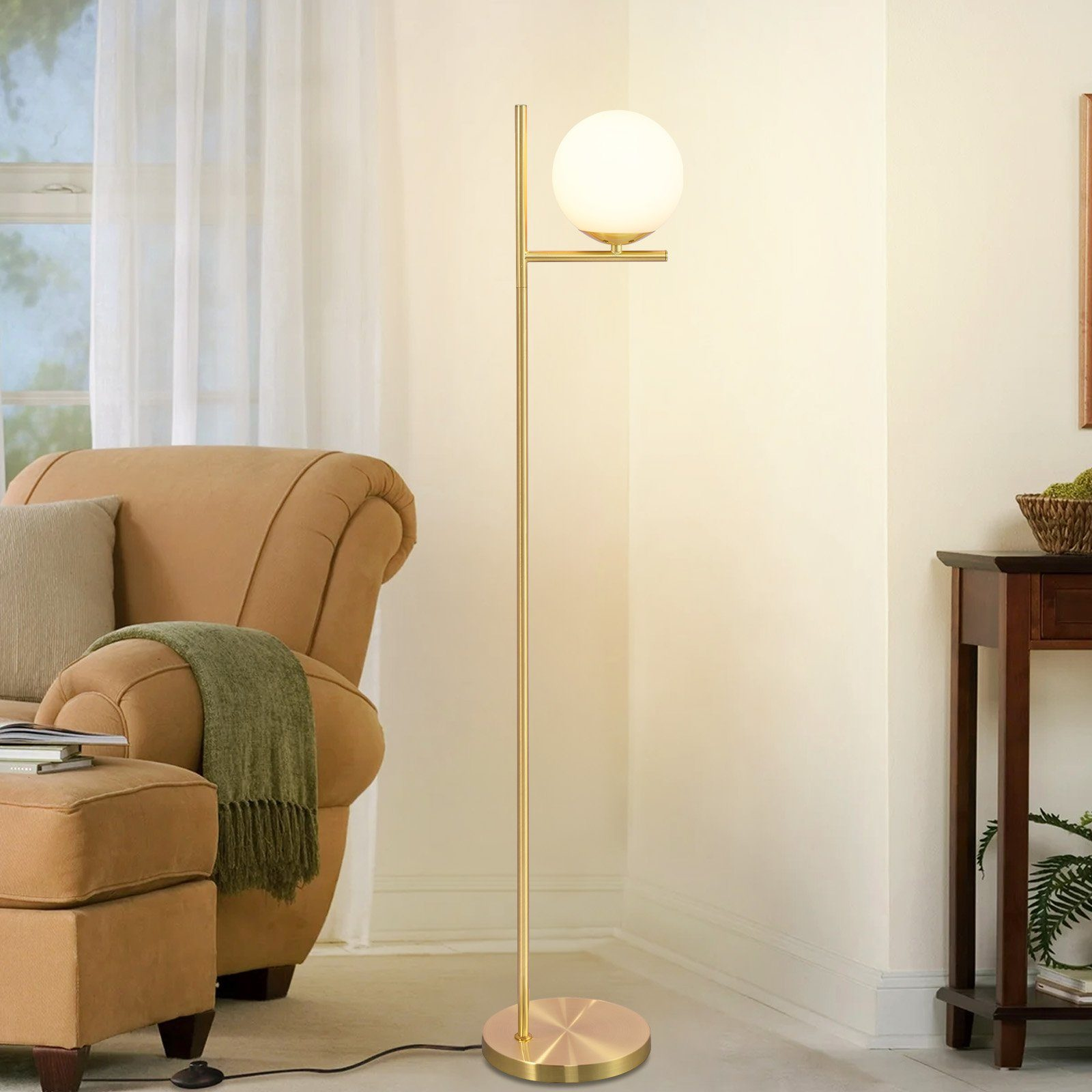 Una lampada da terra dorata con una lampadina bianca a forma di globo è accanto a una poltrona beige.