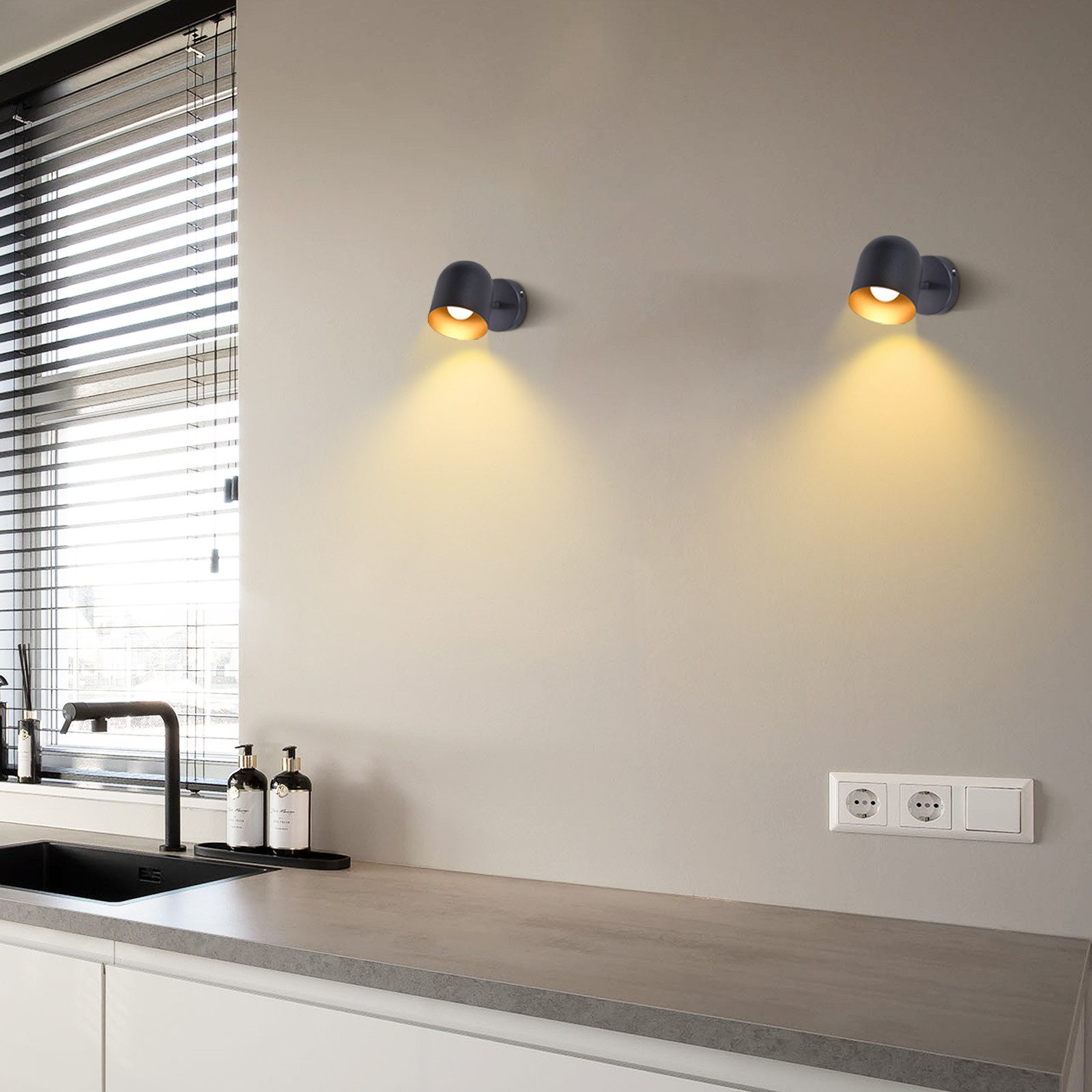 Due lampade da parete nere con luce color oro che brillano su un muro grigio.