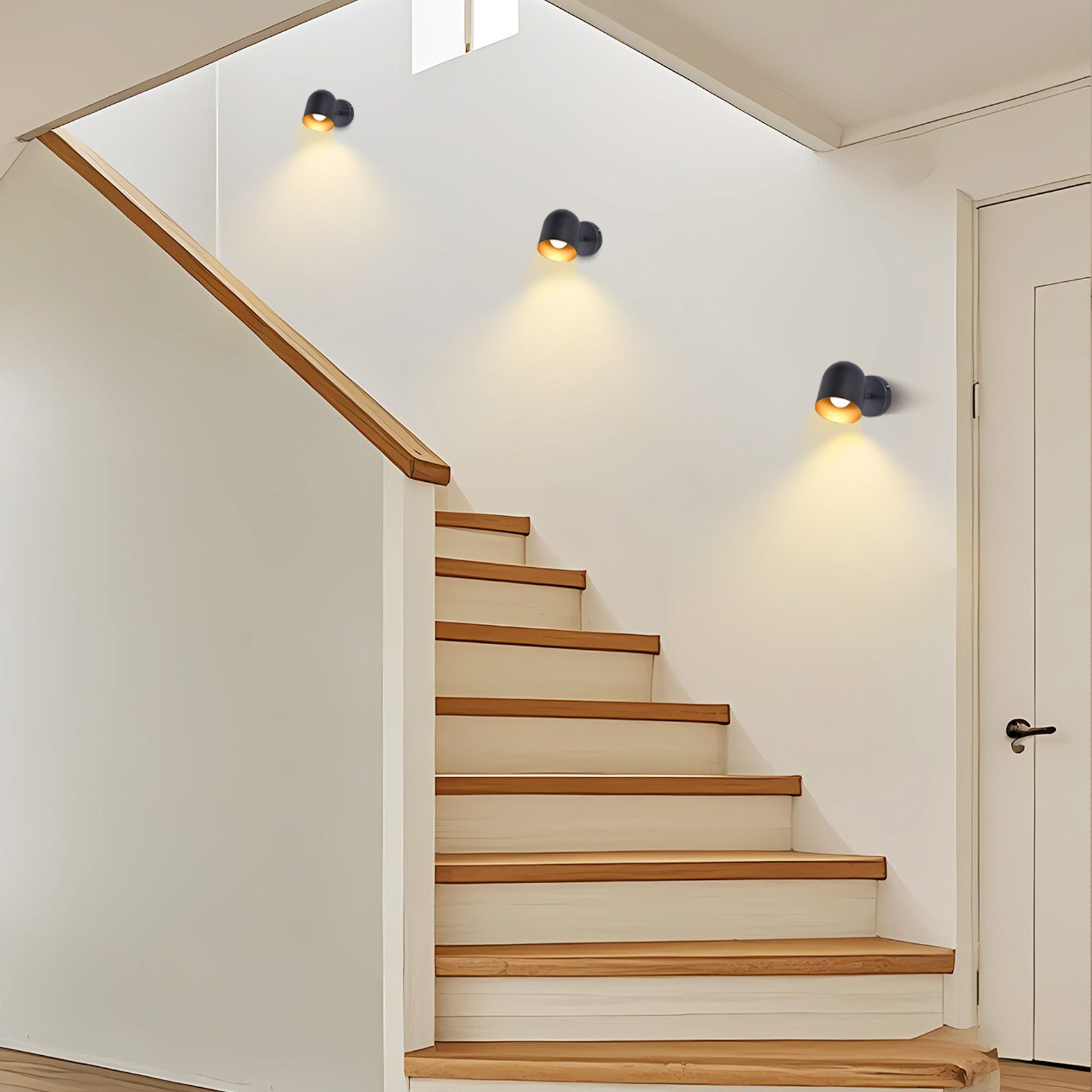 Scala con tre applique nere. Muri bianchi e gradini in legno. Luce gialla.