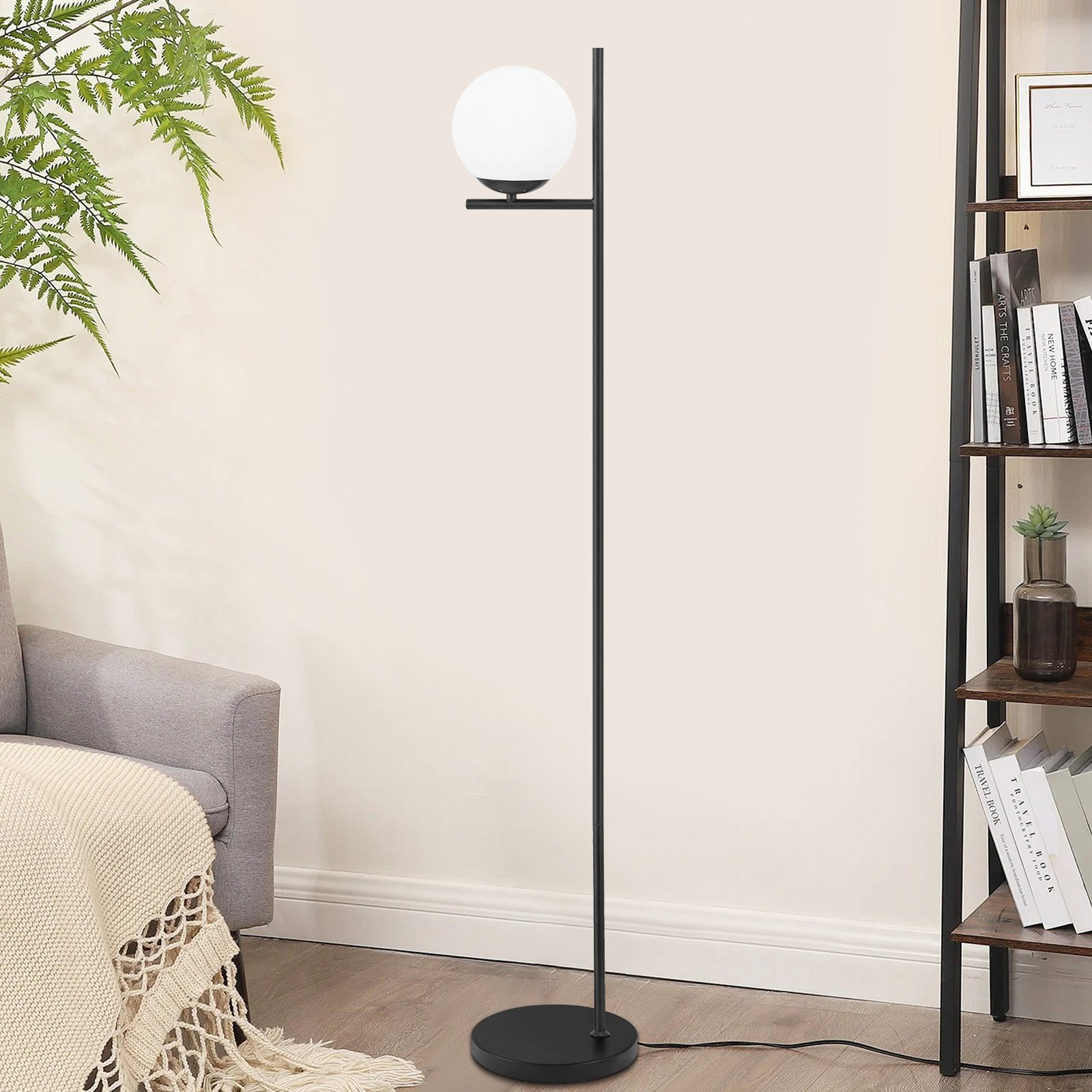 Una lampada da terra nera con paralume a globo bianco, accanto a una libreria e un divano grigio.
