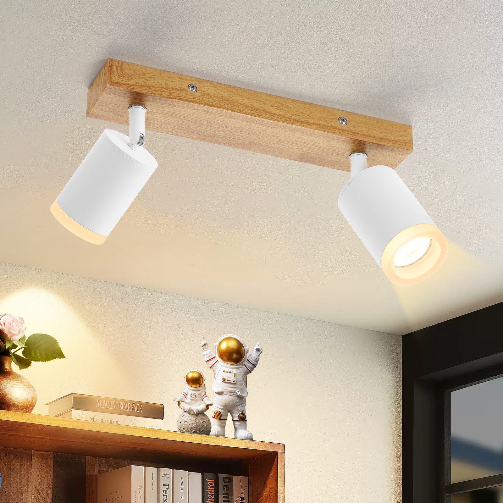 Lampada da soffitto con due faretti bianchi su una trave di legno, con una mensola e figure sullo sfondo.