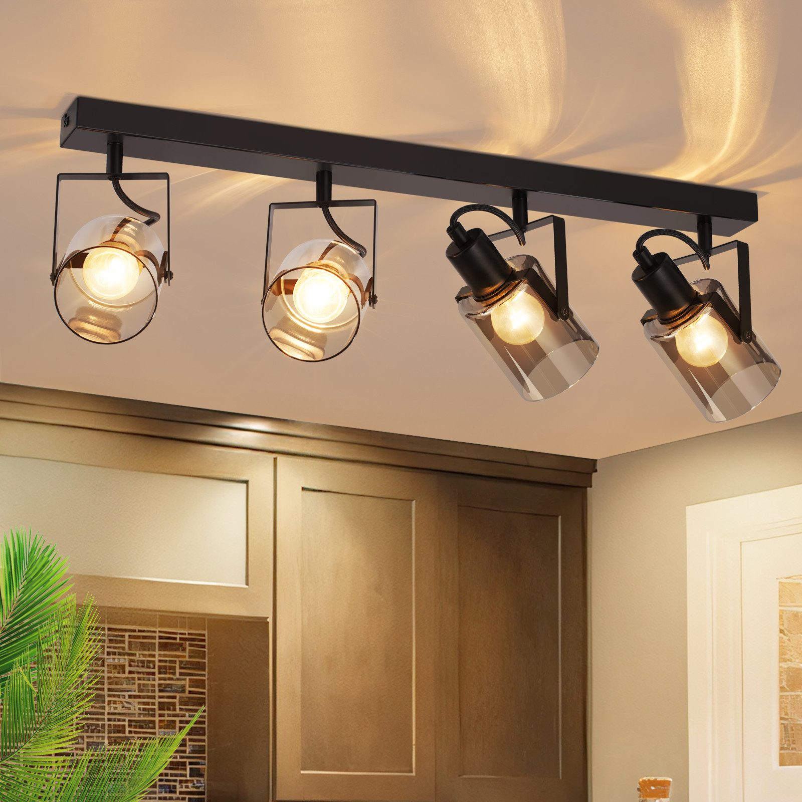 Quattro faretti neri con paralumi in vetro su un soffitto, che illuminano i pensili della cucina.
