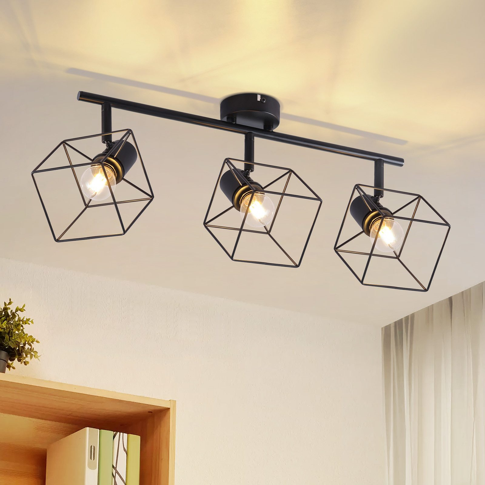 Apparecchio di illuminazione a soffitto con tre lampade racchiuse in telai metallici geometrici. Sfondo bianco del soffitto.