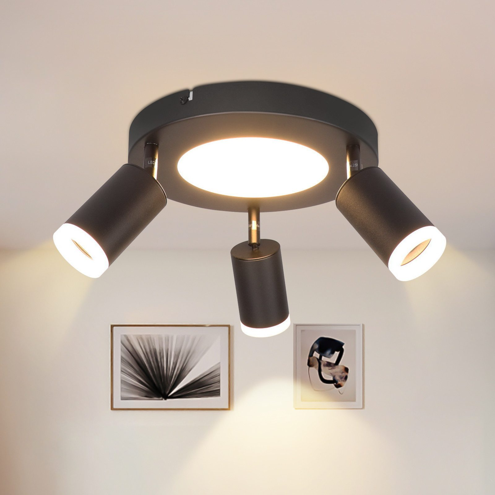 Faretti da soffitto neri con tre luci, incorniciati da due quadri su un muro bianco.