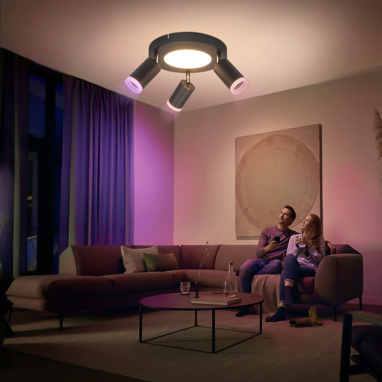 Un soggiorno con un divano e un apparecchio di illuminazione che illumina con luci viola, rosa e bianche.