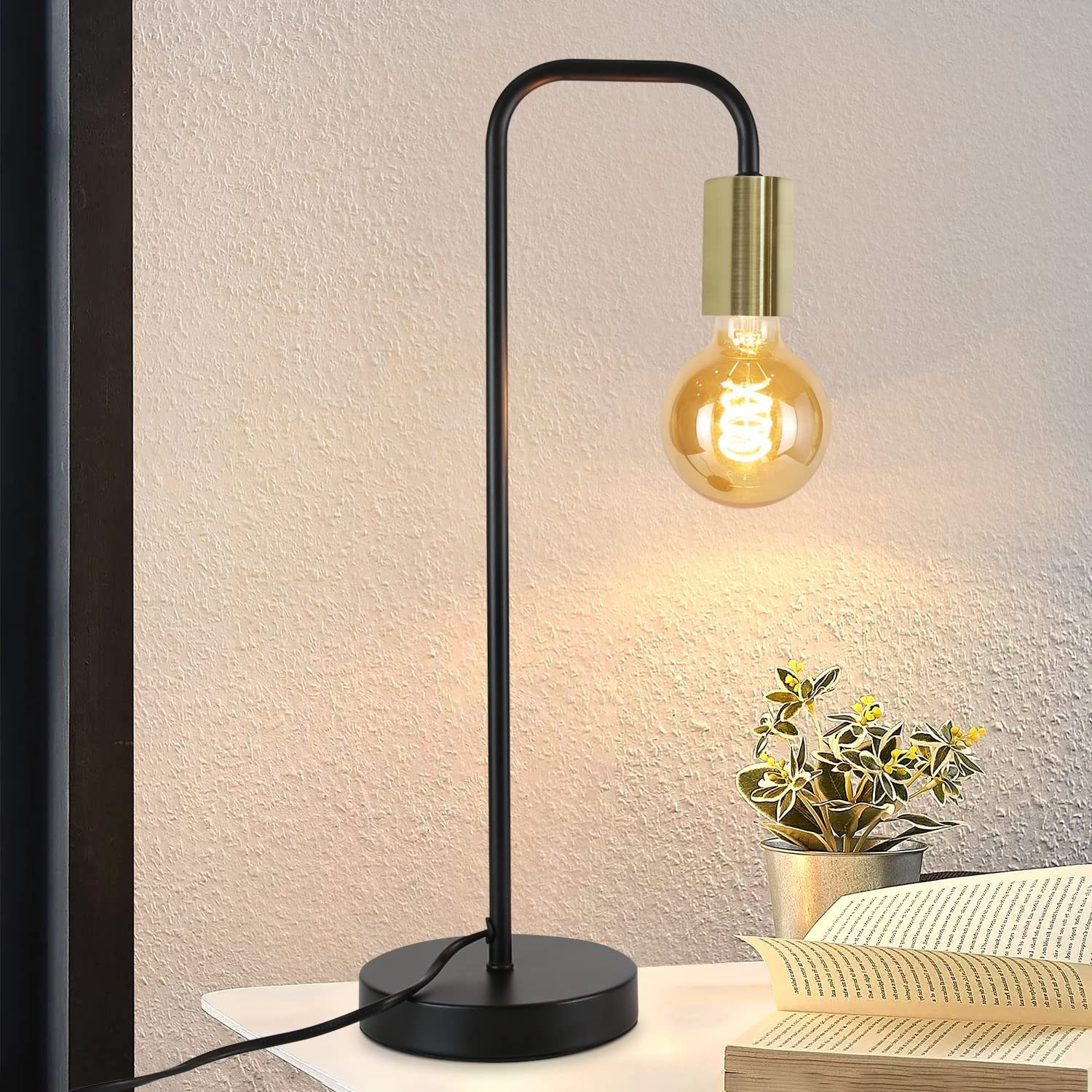 Lampada da scrivania nera e oro con lampadina e libro. La lampada è su un tavolo bianco.