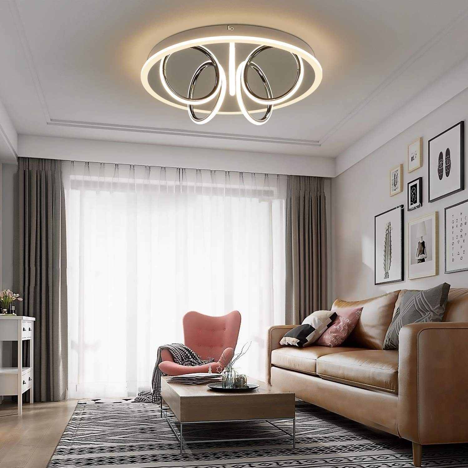 Un soggiorno con una moderna lampada da soffitto, un divano, una poltrona rosa e quadri sul muro.